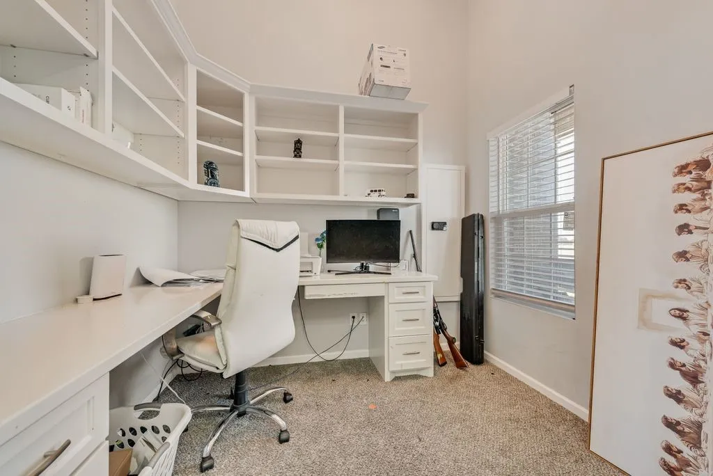 Built-in shelving, integrated desk, window with blinds, and neutral​​‌​​​​‌​​‌‌​‌‌​​​‌‌​‌​‌​‌​​​‌​​ carpeting