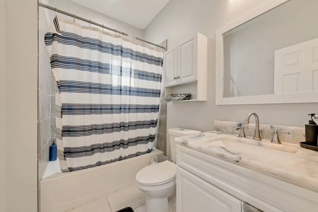 Bathroom featuring a white vanity with an integrated sink, white cabinetry, a built-in bathtub with tiled surround, and a wall-mounted mirror