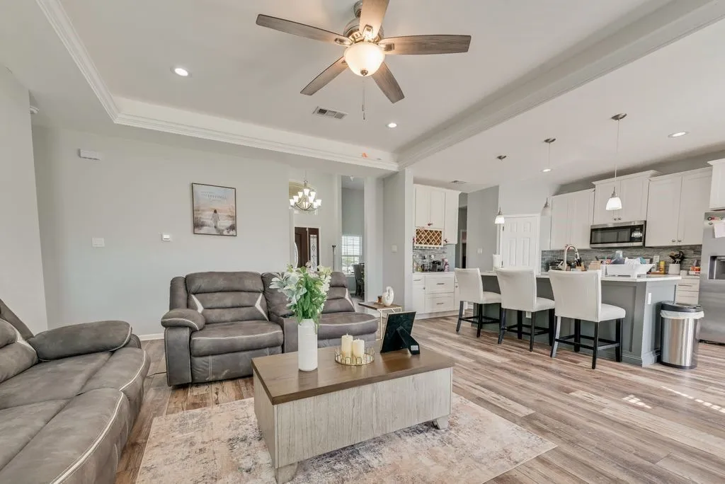 Open-concept living space with wood-finish flooring, crown molding, a ceiling fan, and recessed lighting