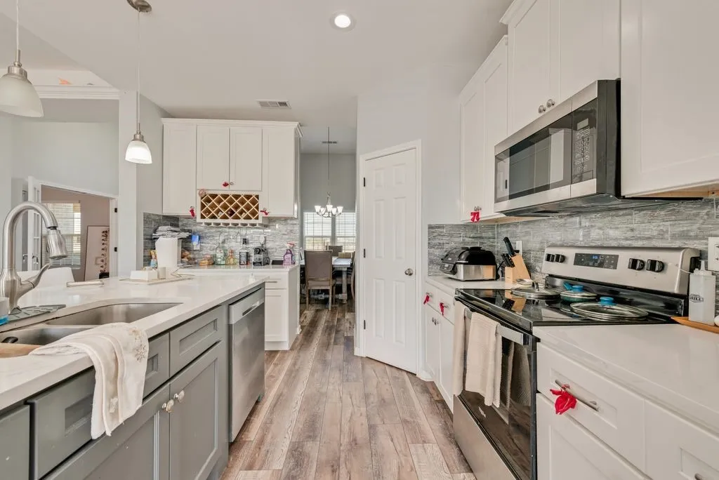 Kitchen featuring a center island with sink, white upper and gray lower cabinetry, stainless steel appliances, wood-finish flooring, and a tile backsplash