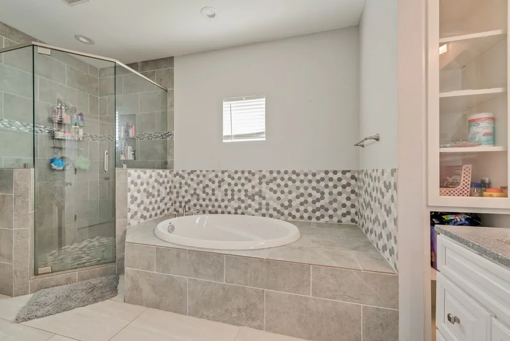 Glass-enclosed shower with tile surround, built-in soaking tub with mosaic tile accents, and built-in white cabinetry with glass display doors