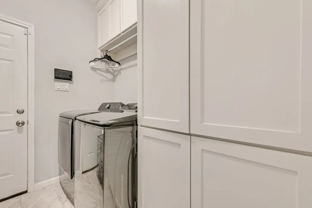 Laundry area featuring white shaker-style cabinetry, overhead shelving, and light-toned tile flooring
