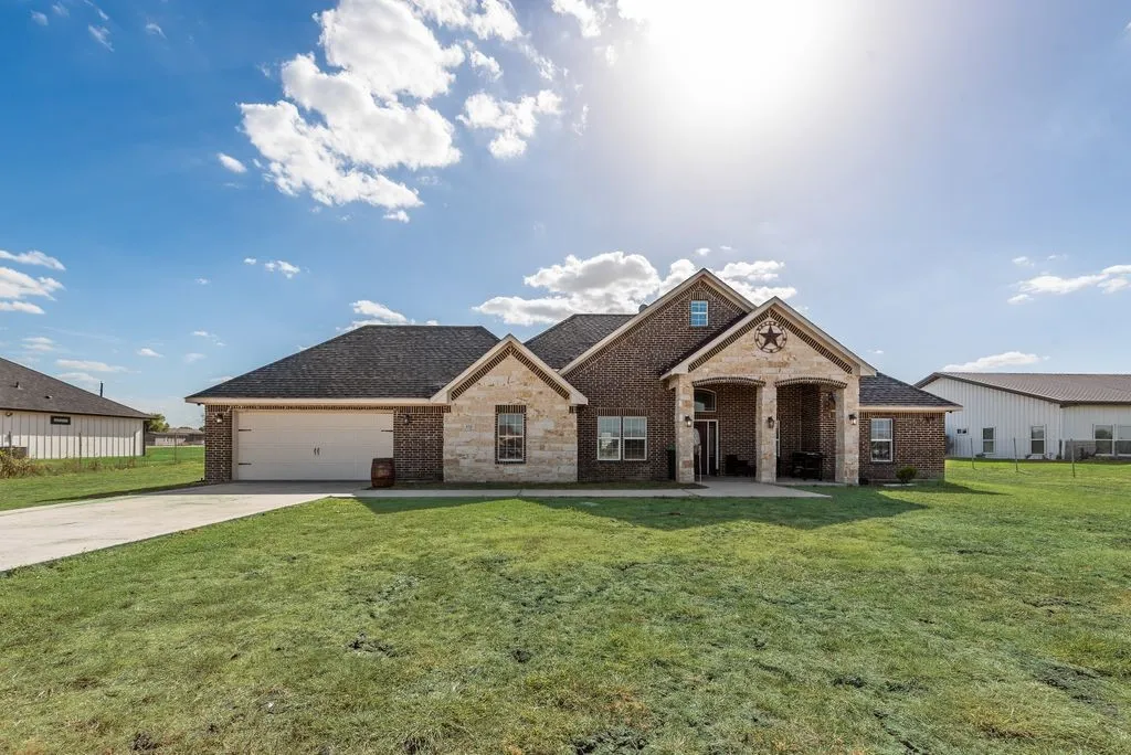 Brick and stone facade, covered front porch, two-car garage, pitched shingle roof, concrete driveway