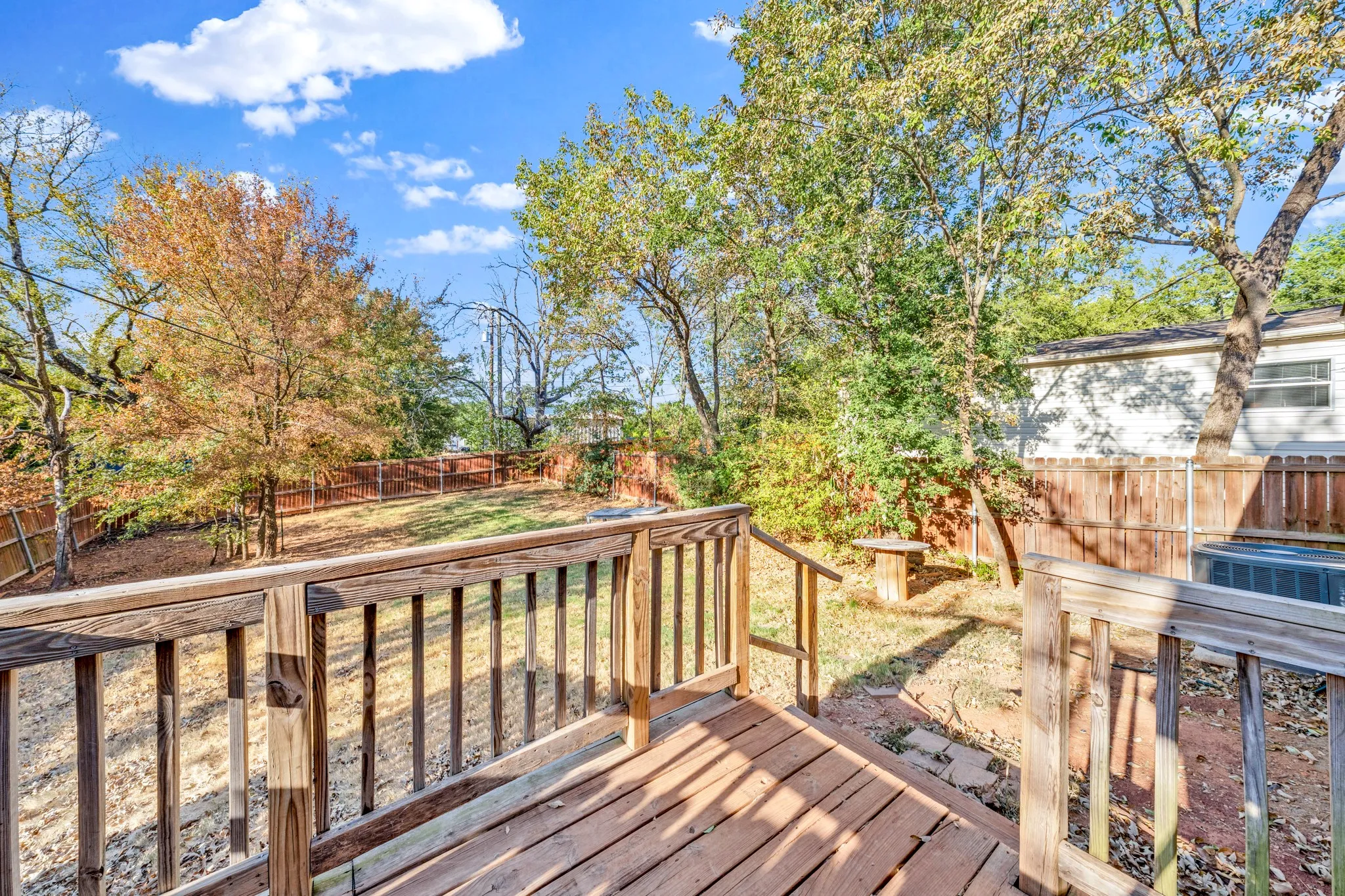 Wood-plank deck with railing overlooking a fenced backyard featuring mature trees
