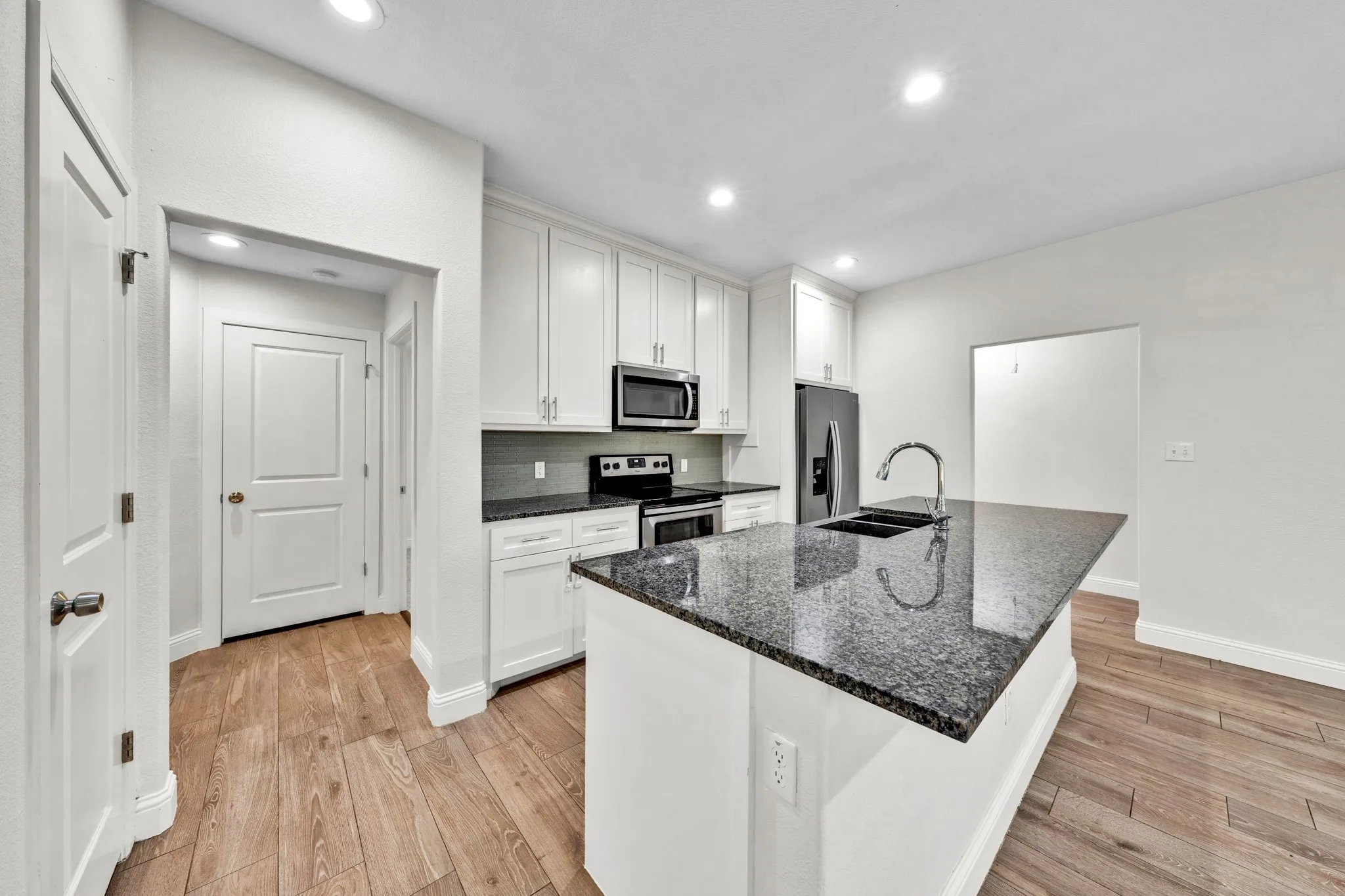 Kitchen featuring wood-finish flooring, white cabinetry, dark stone countertops, a large island with an integrated sink, and recessed lighting