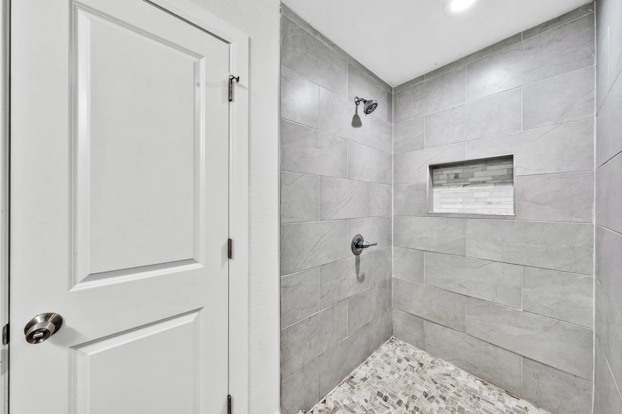 Tiled shower with a niche, mosaic tile flooring, and a rainfall showerhead