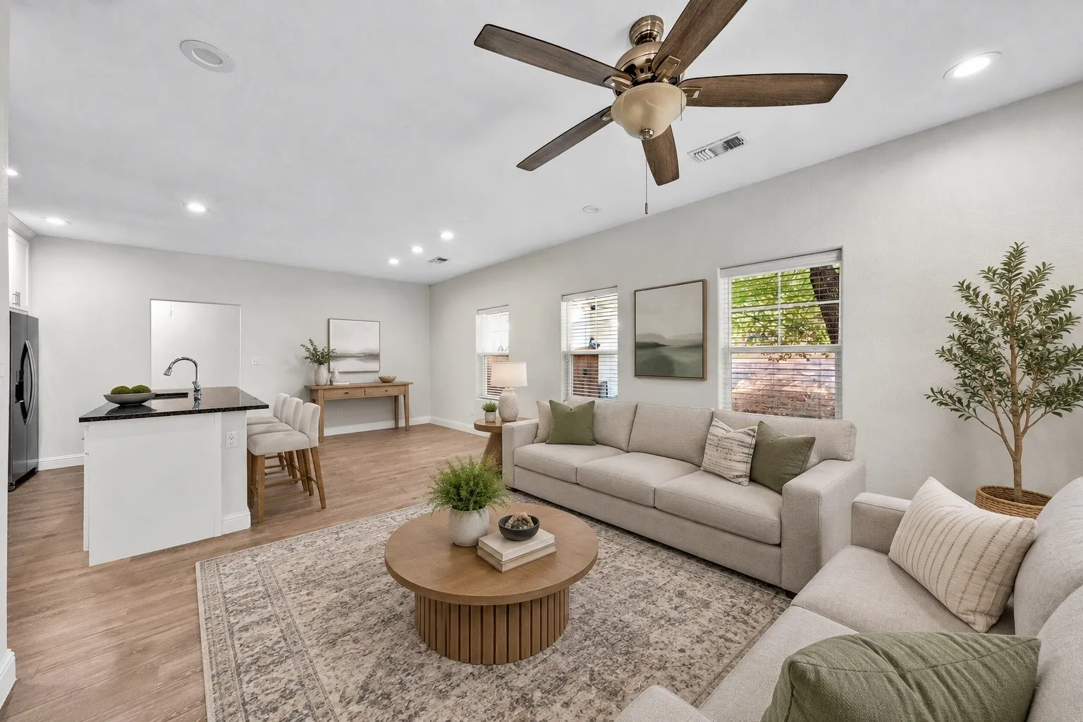 Wood-finish flooring, recessed lighting, ceiling fan, kitchen island with dark countertop, and multiple windows