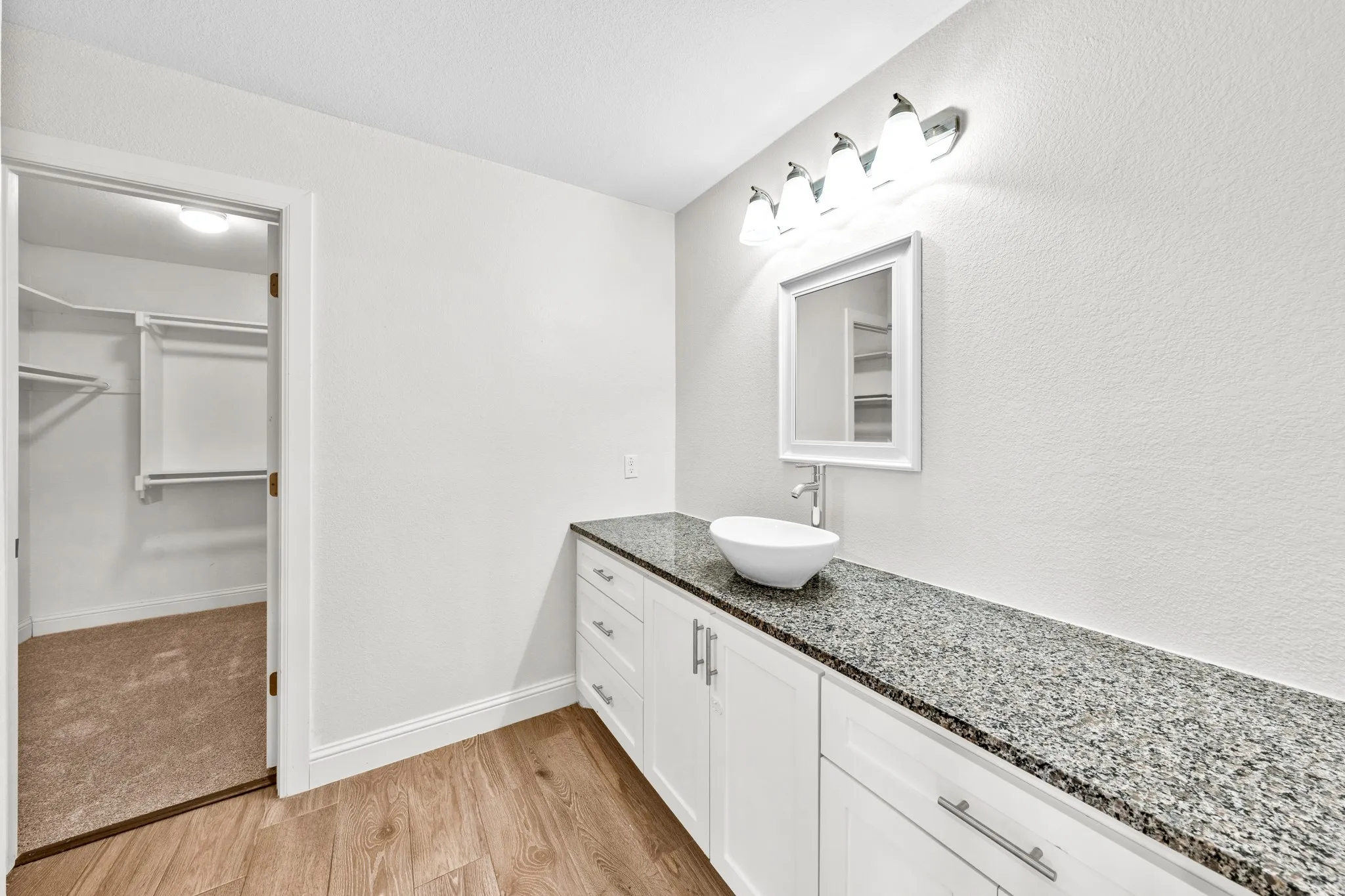 White shaker-style vanity with ample storage, a speckled countertop, and a vessel sink