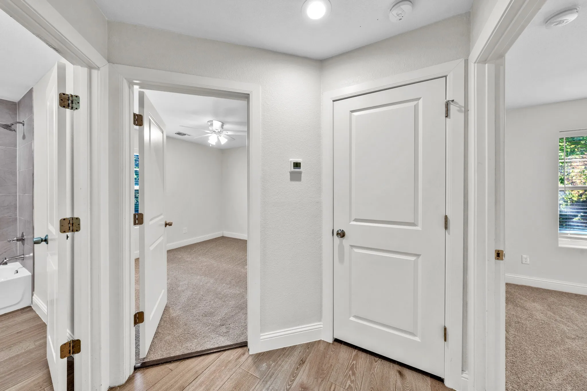 Wood-finish flooring, white panel doors, recessed ceiling lighting, and a thermostat