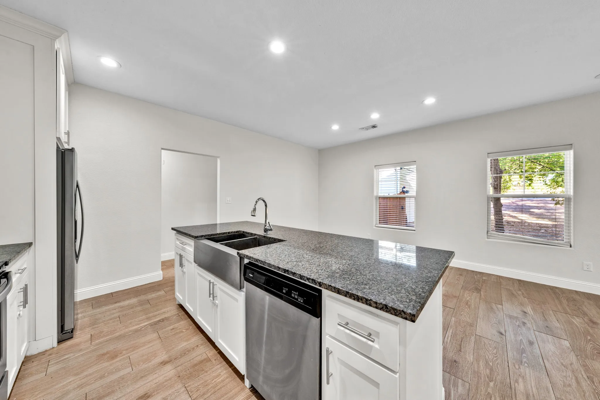 Kitchen island with a farmhouse sink, stainless steel appliances, granite countertops, and wood-finish flooring