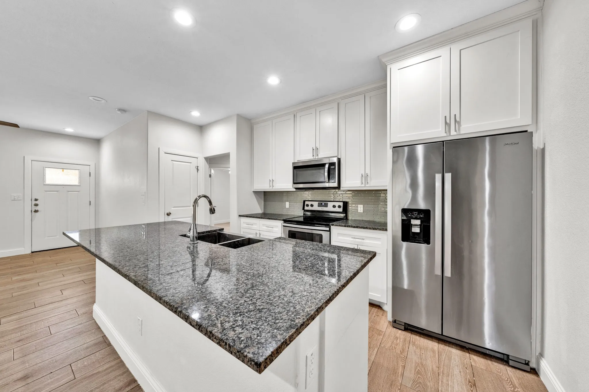 Kitchen featuring a large island with a double basin sink, stainless steel appliances, white cabinetry, and wood-finish flooring