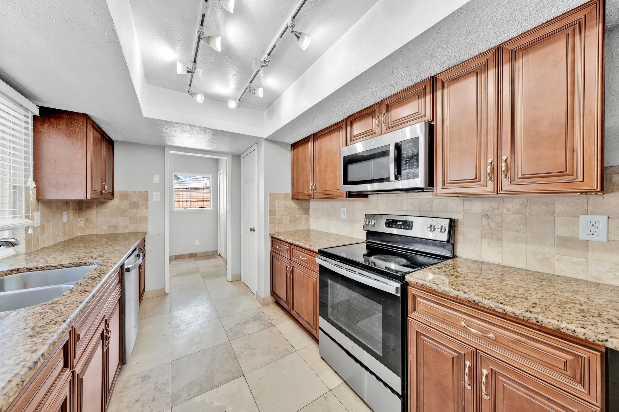 Kitchen featuring abundant cabinetry, stone-finish countertops, stainless steel appliances, a double basin sink, and track lighting