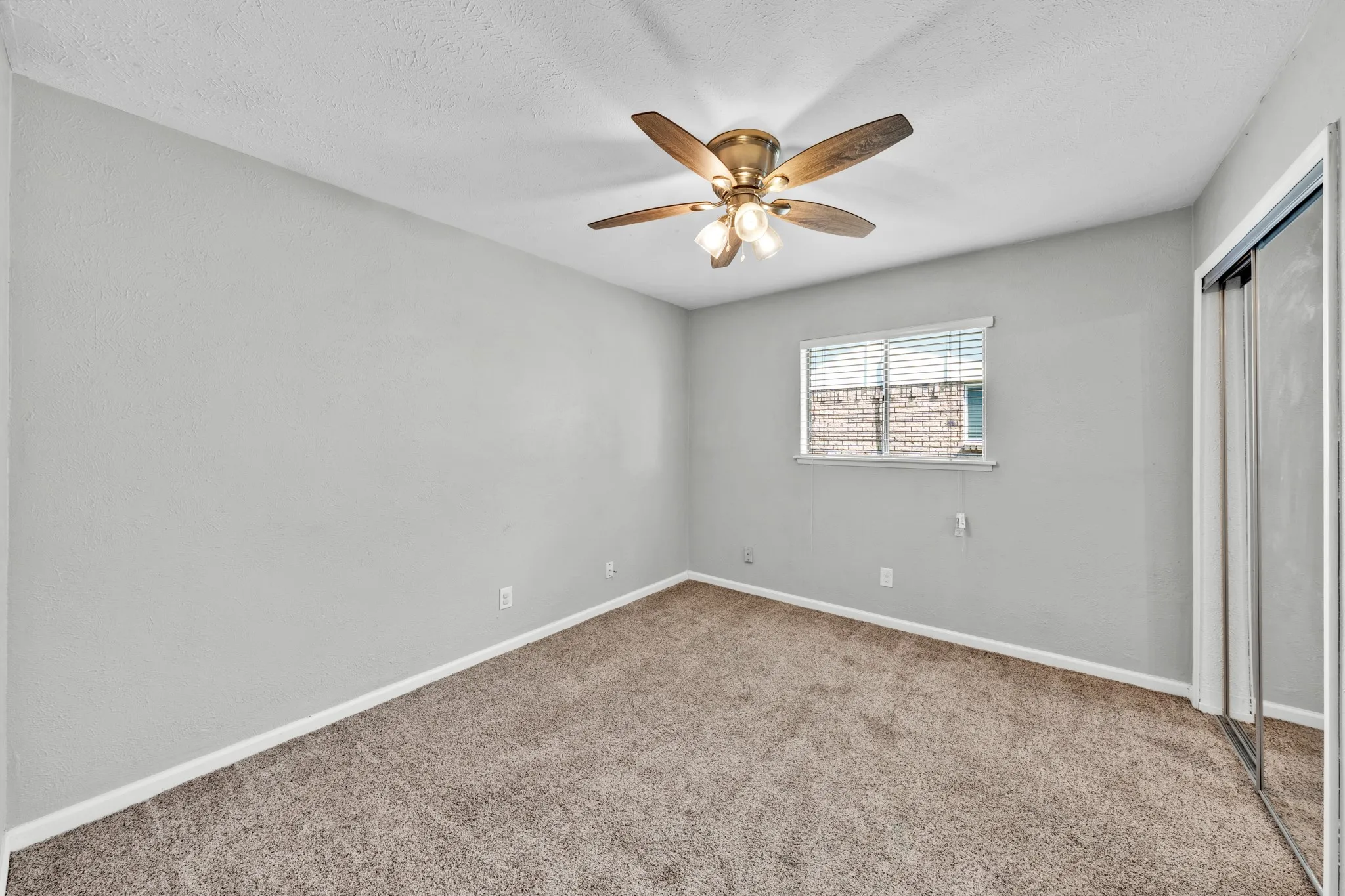 Wall-to-wall carpeting, window with horizontal blinds, built-in ceiling fan with integrated lighting, and mirrored sliding closet doors