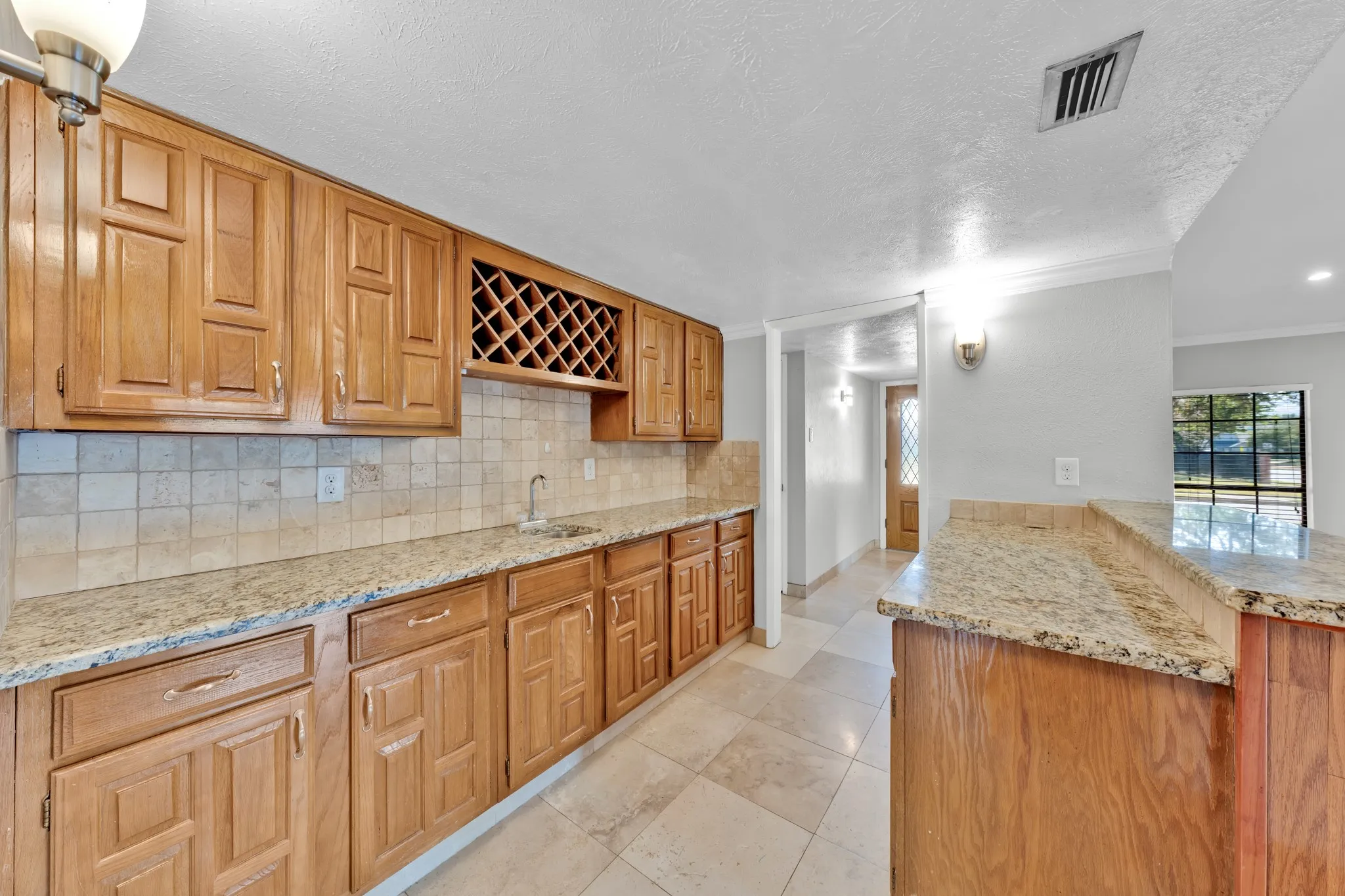 Wood-finish cabinetry with a built-in wine rack, light-toned tile backsplash, and granite countertops