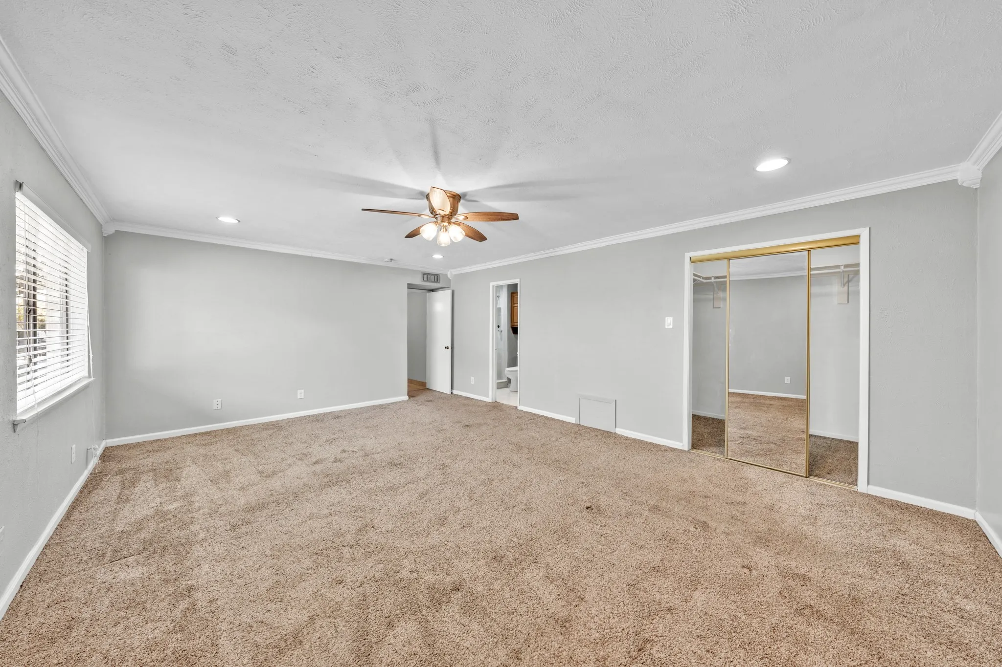 Expansive carpeted room featuring a ceiling fan, recessed lighting, crown molding, and sliding mirrored closet doors