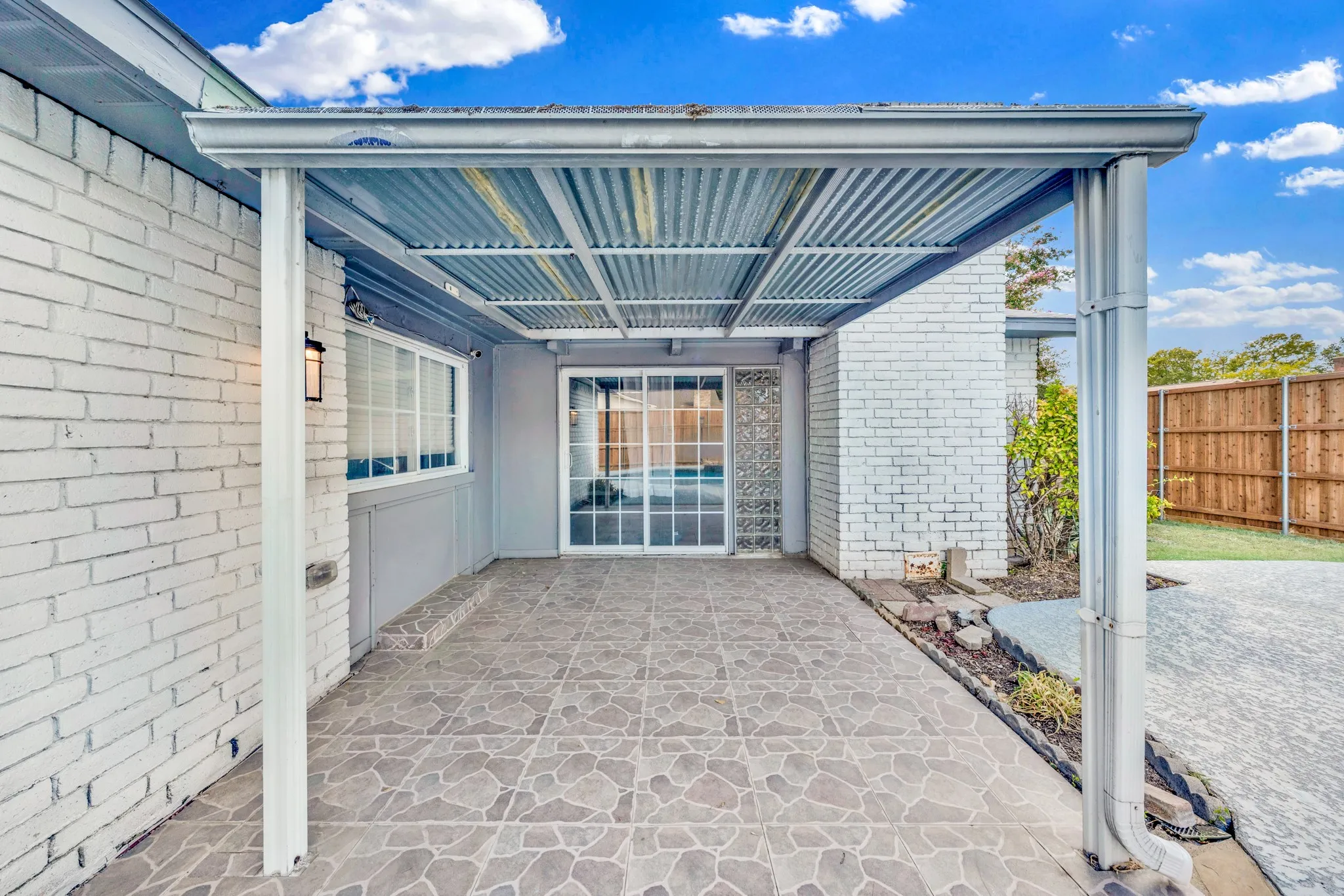 Covered patio featuring a corrugated metal roof, patterned tile flooring, and white painted brick exterior walls