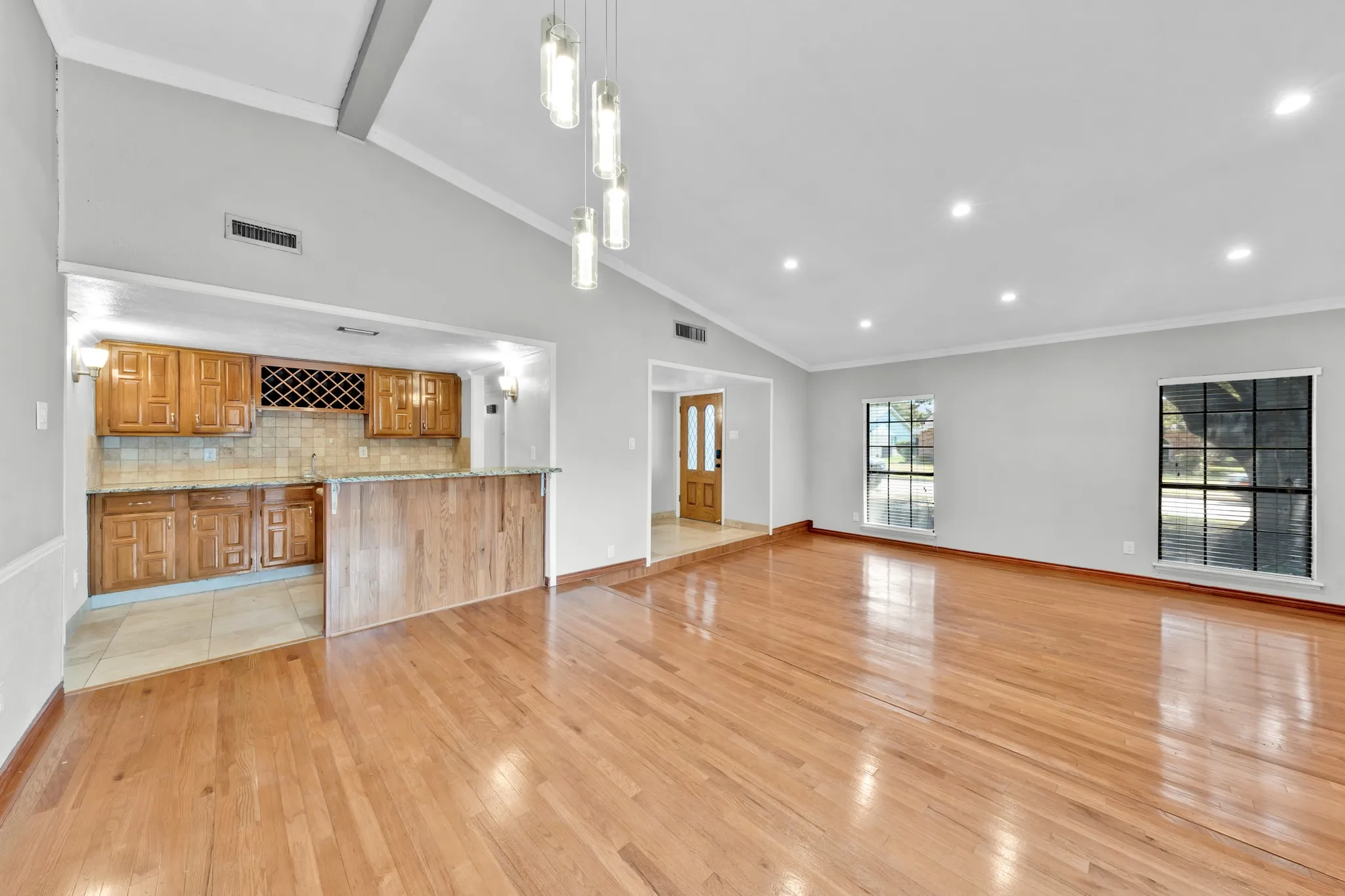 Vaulted ceiling with pendant lighting, recessed lighting, wood-finish flooring, wood cabinetry, and a built-in wet bar