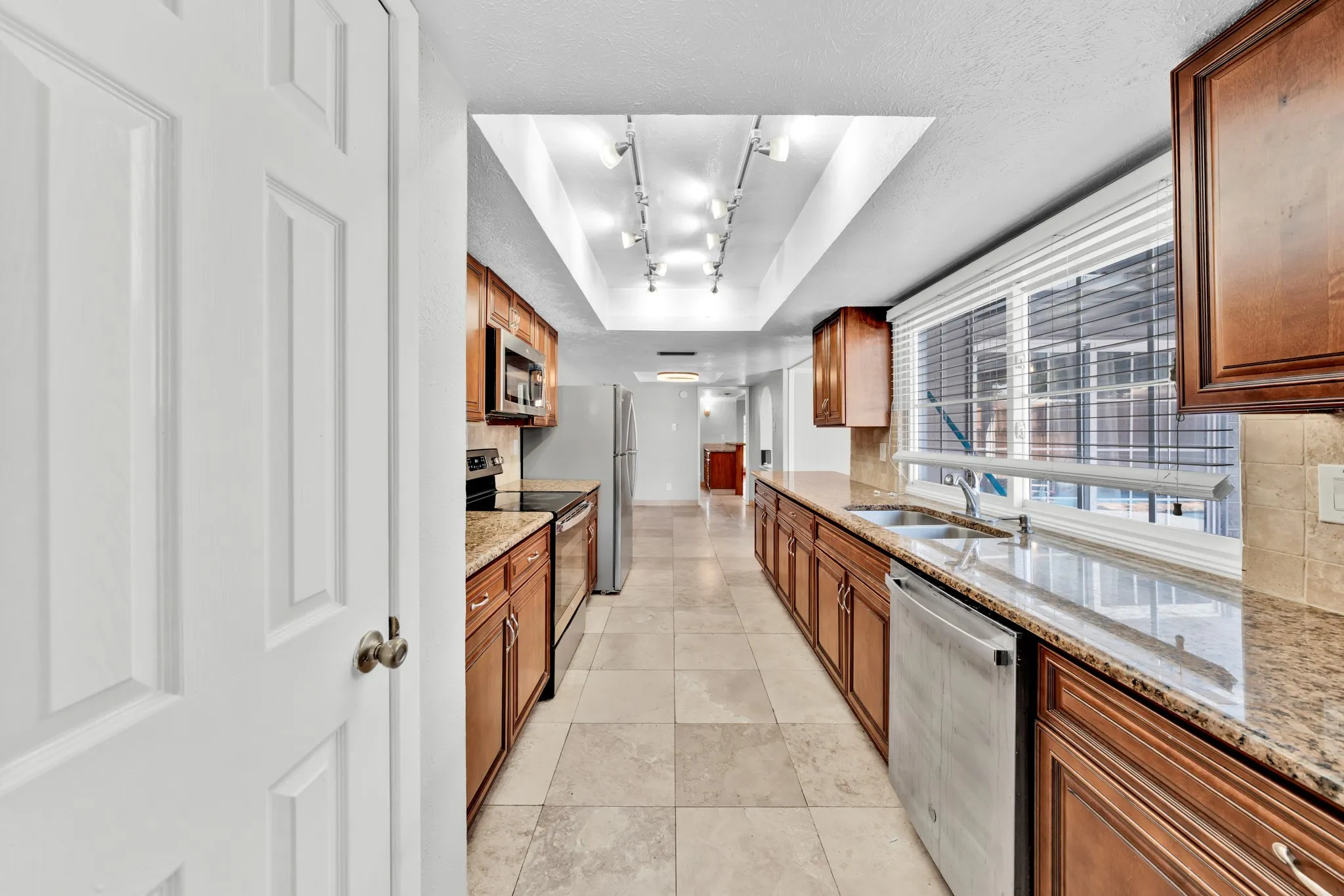 Galley kitchen featuring wood cabinetry, stone countertops, stainless steel appliances, and tiled flooring