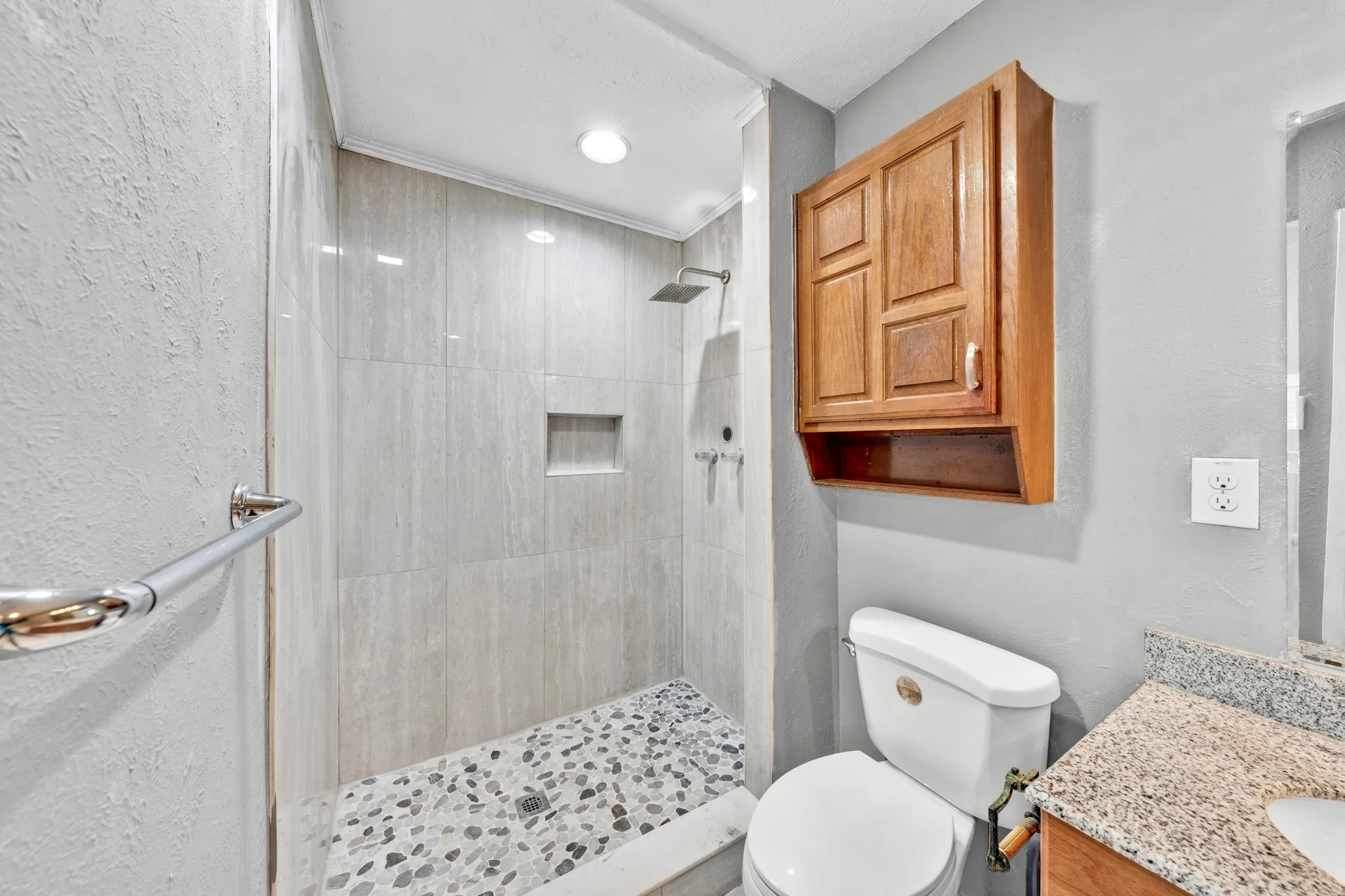 Walk-in shower with stone tile flooring, recessed niche, and overhead rain shower