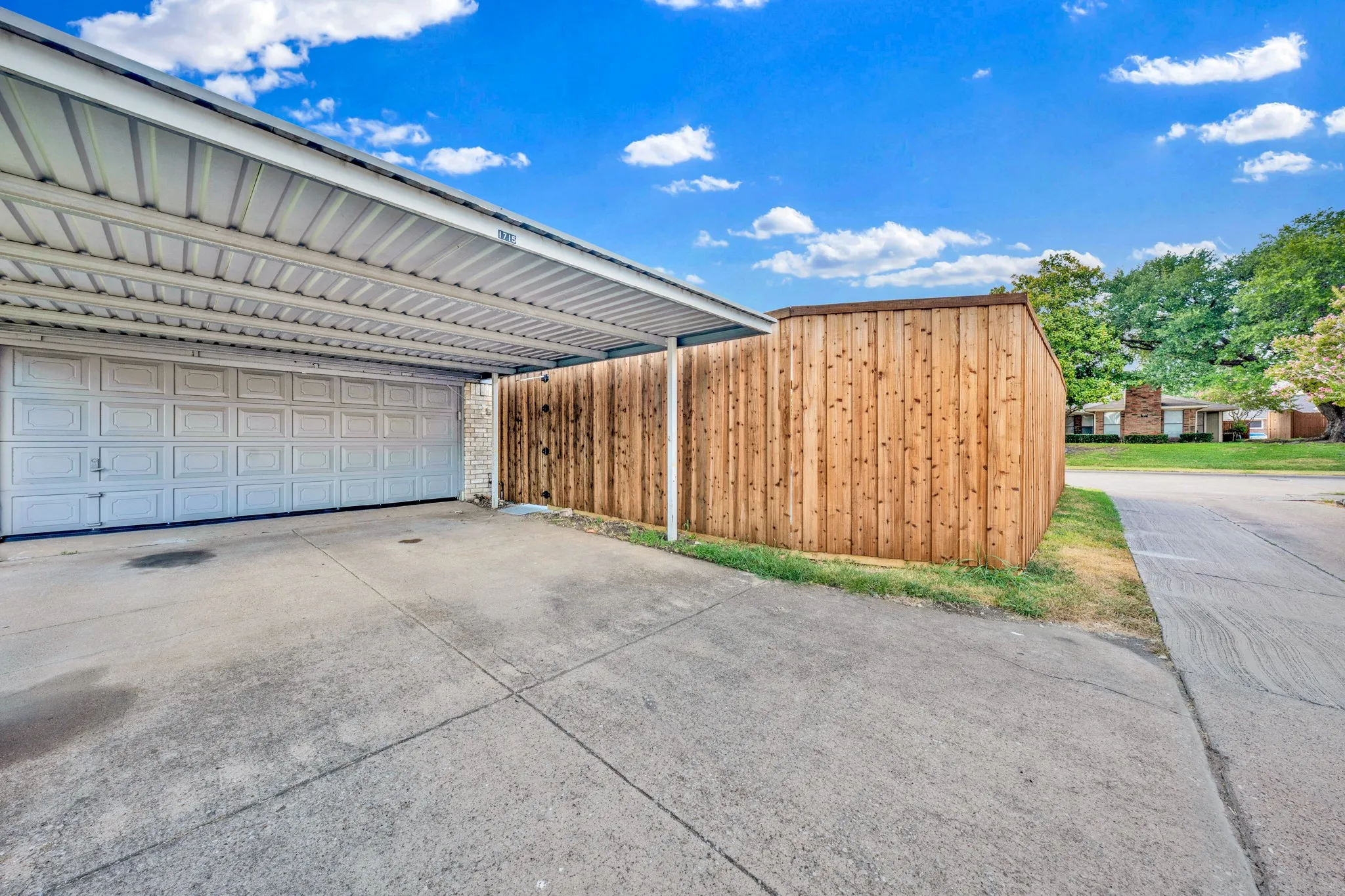 Attached carport with a corrugated metal roof, a two-car garage door, and a concrete driveway