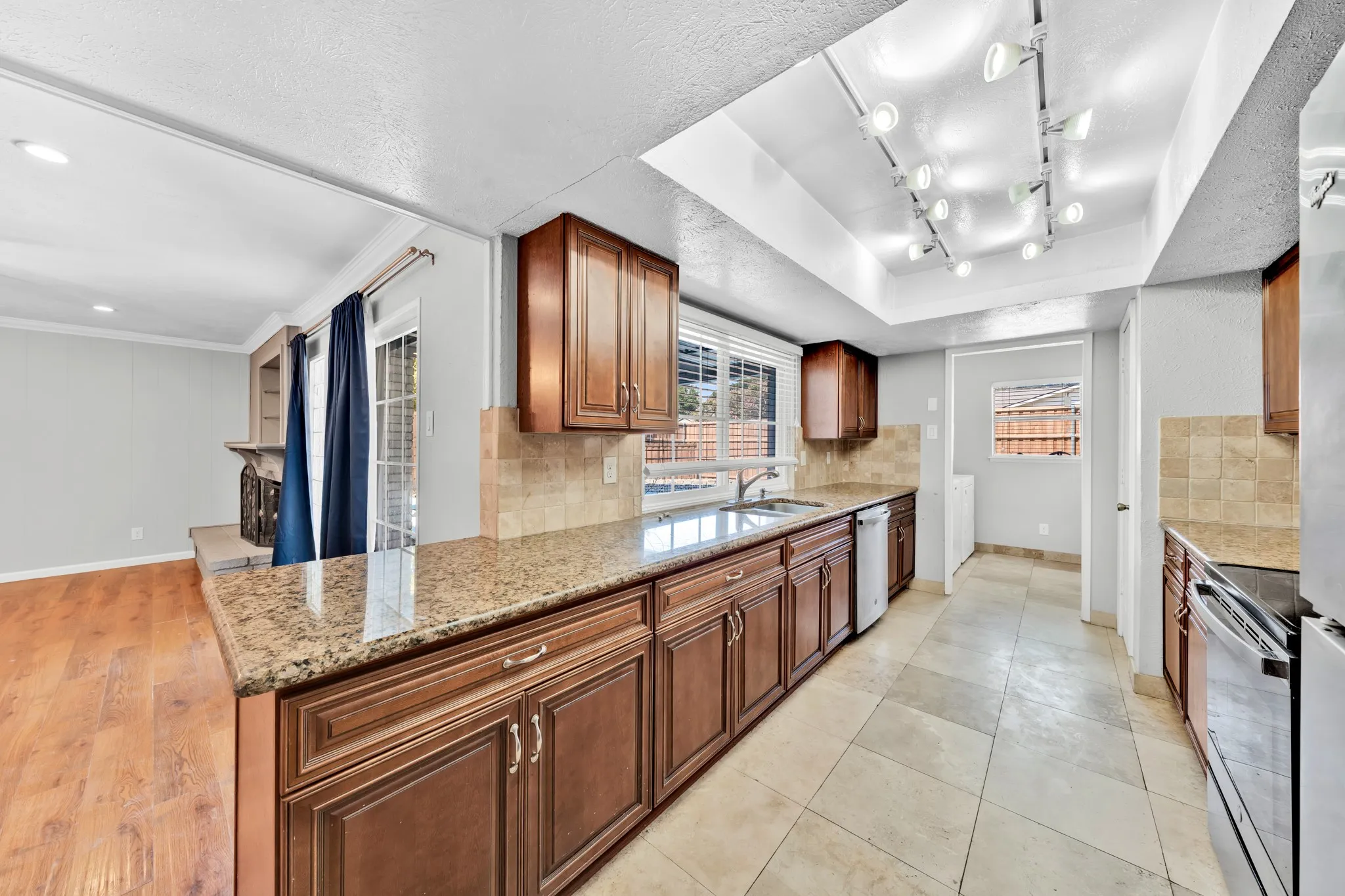 Kitchen featuring wood cabinetry, light-toned tile flooring, granite countertops, and track lighting