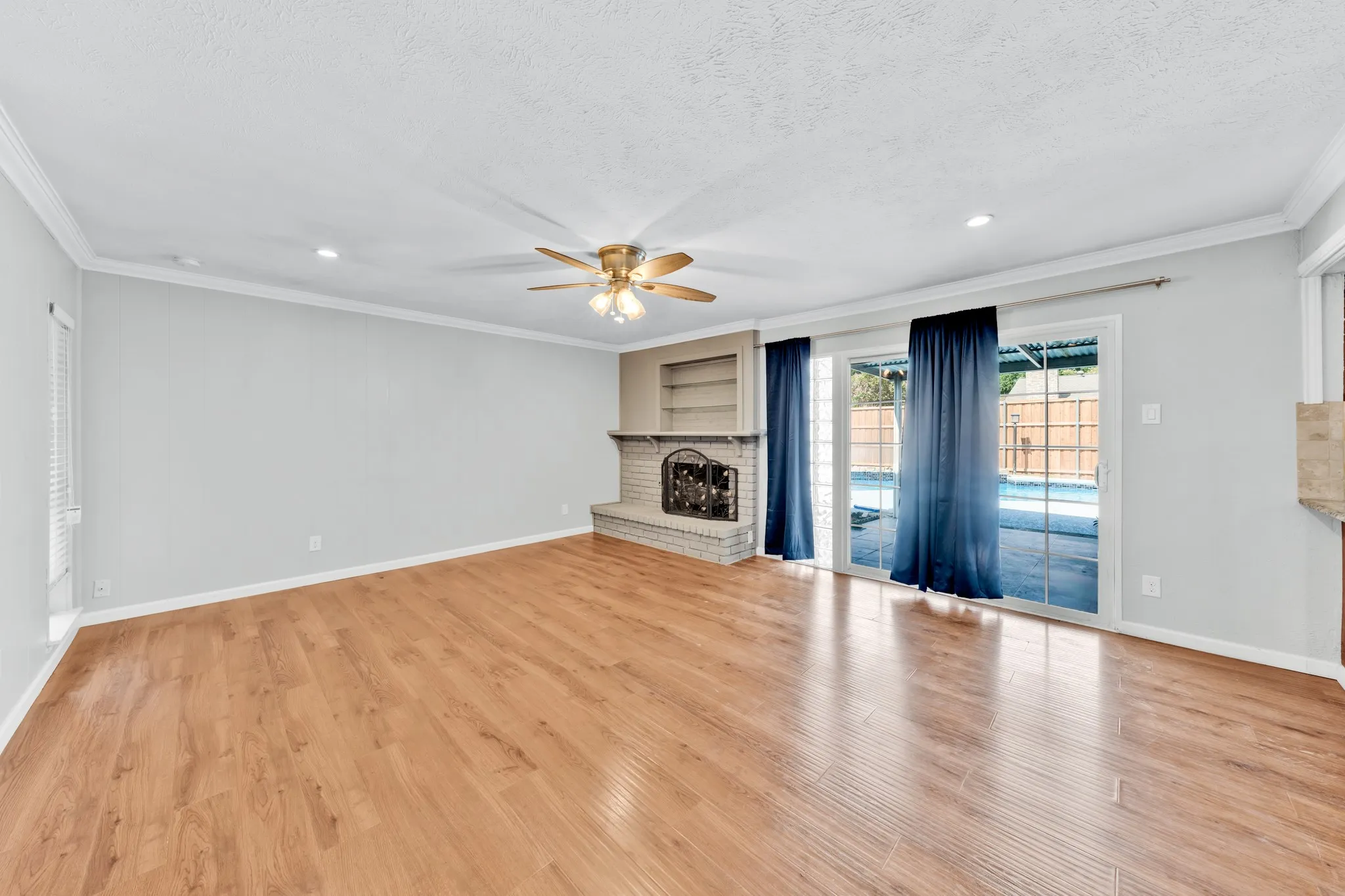 Spacious living area featuring wood-finish flooring, a brick fireplace with built-in shelving, and a ceiling fan