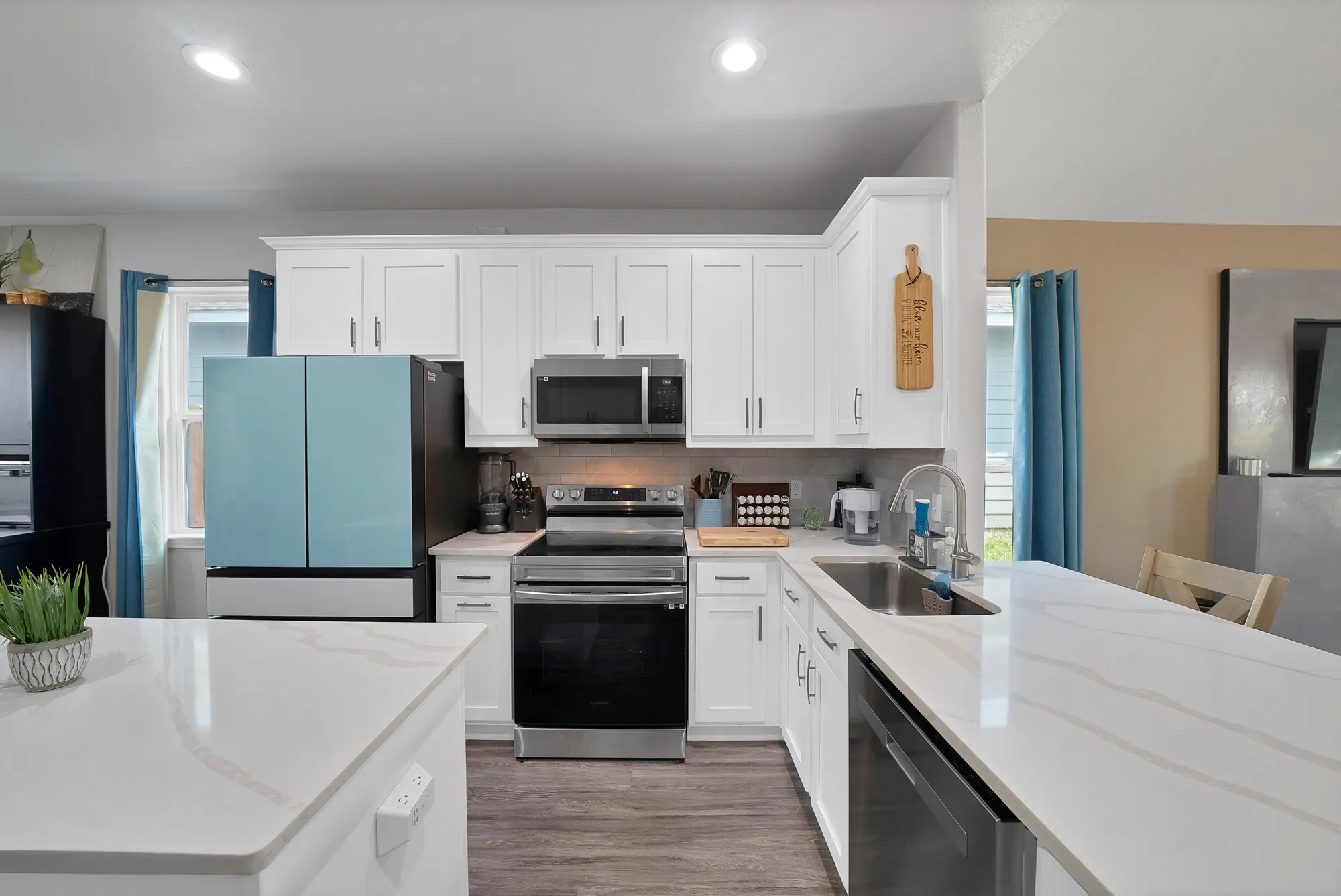 White shaker cabinetry, stainless steel appliances, stainless steel undermount sink, quartz countertops, and wood-finish flooring