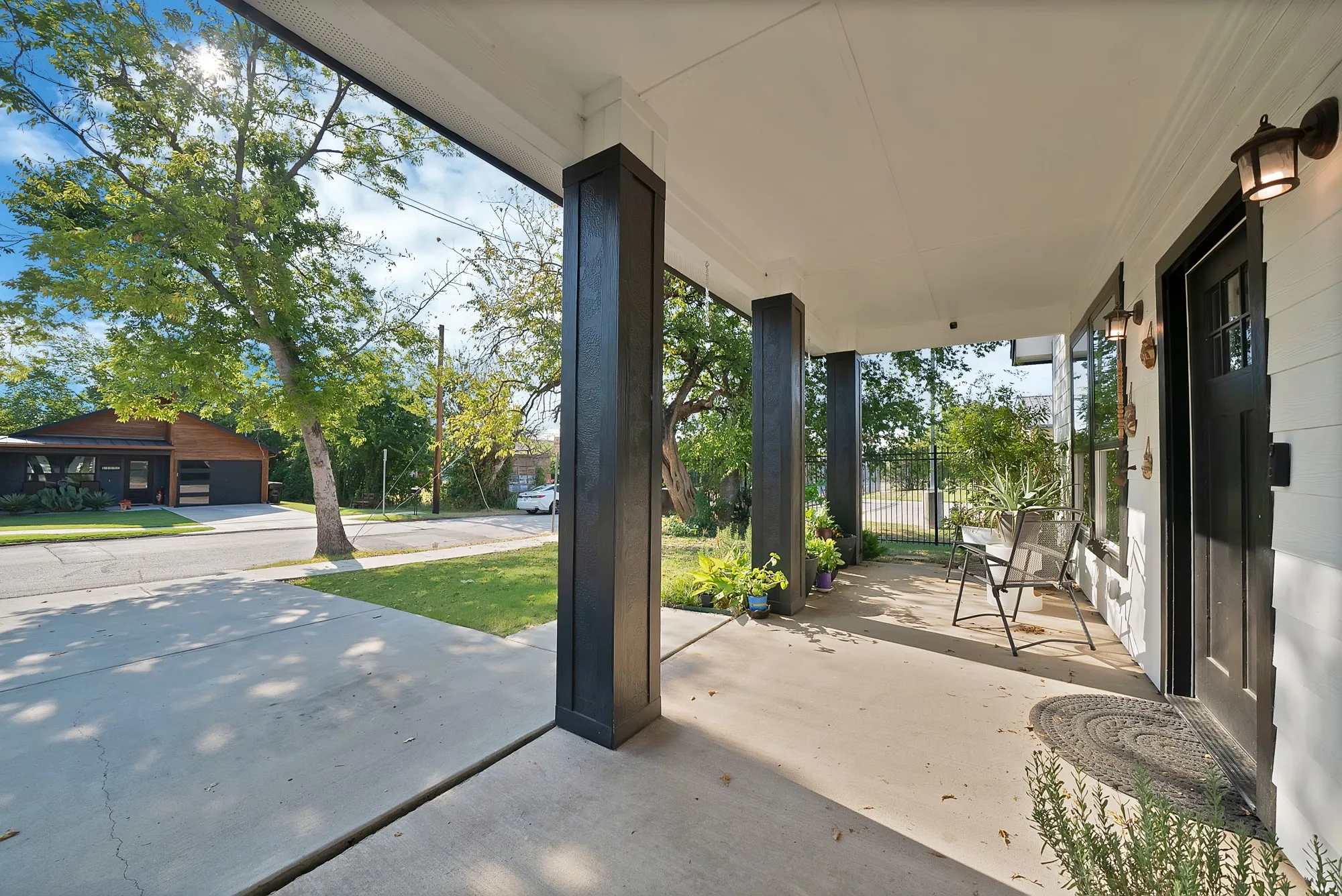 Covered front porch with dark-toned columns, white exterior siding, and a dark-paneled entry door
