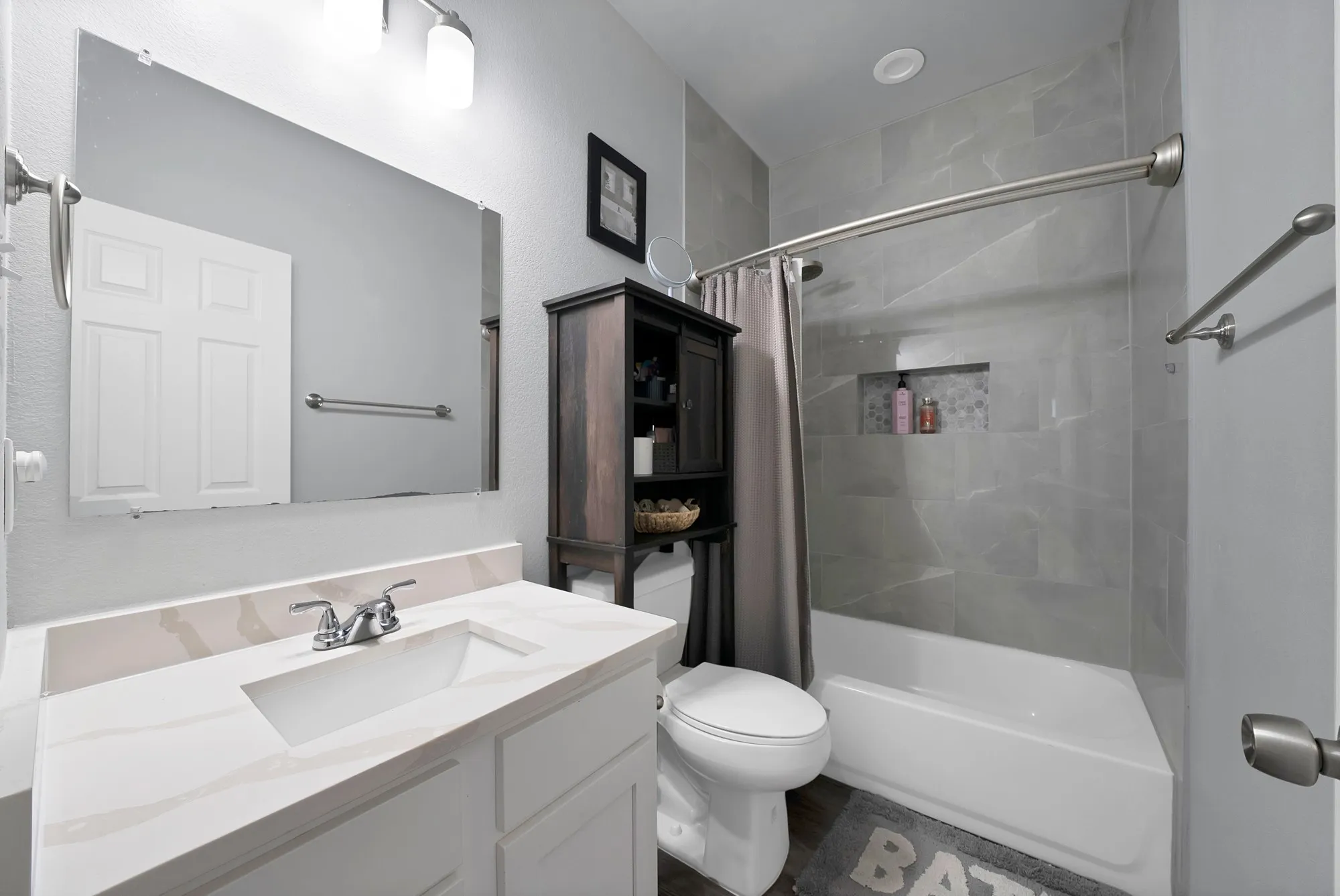 White vanity with integrated sink and chrome faucet, large frameless mirror, and overhead vanity lighting
