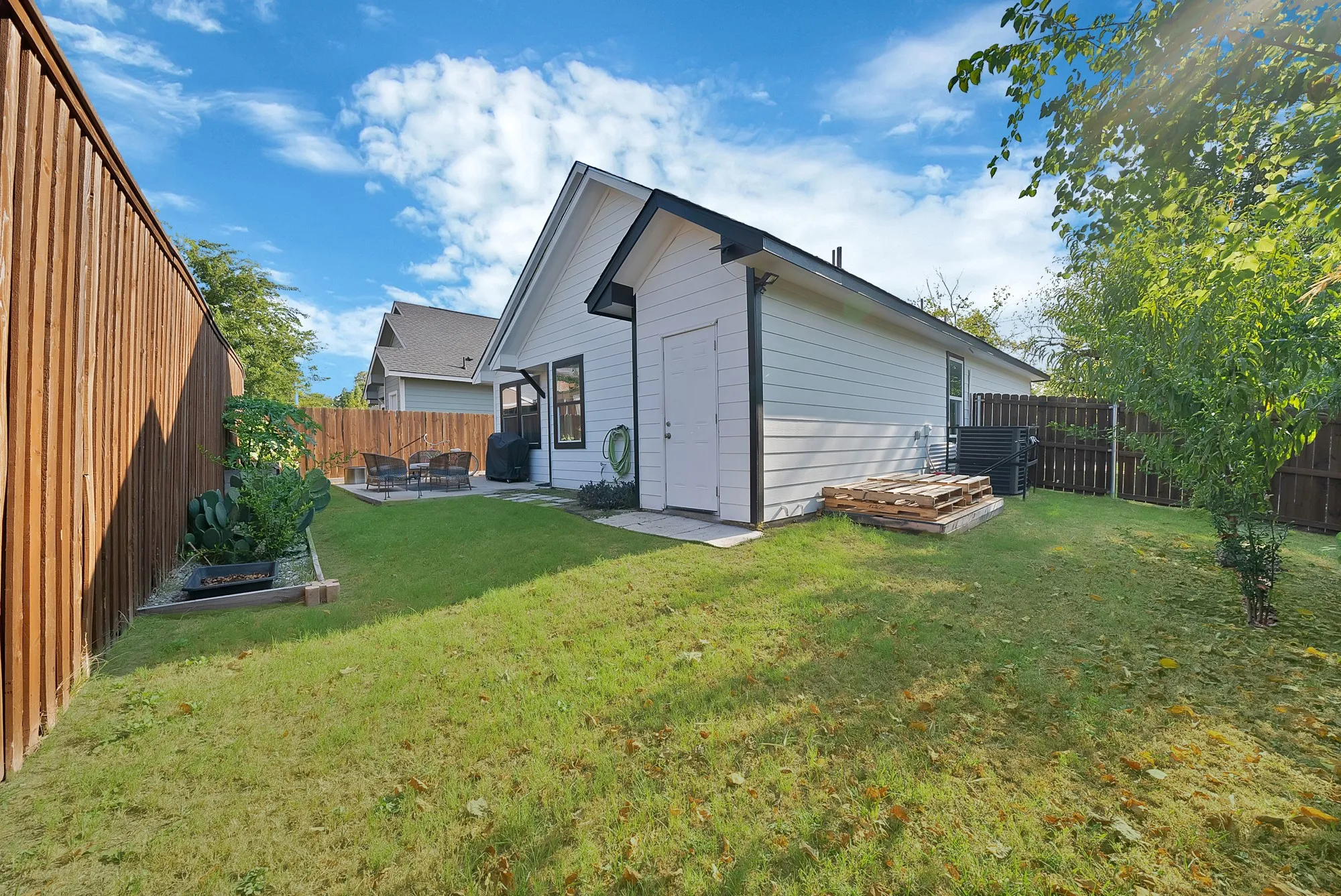 Fenced backyard featuring a patio area, mature foliage, and a shed with white siding
