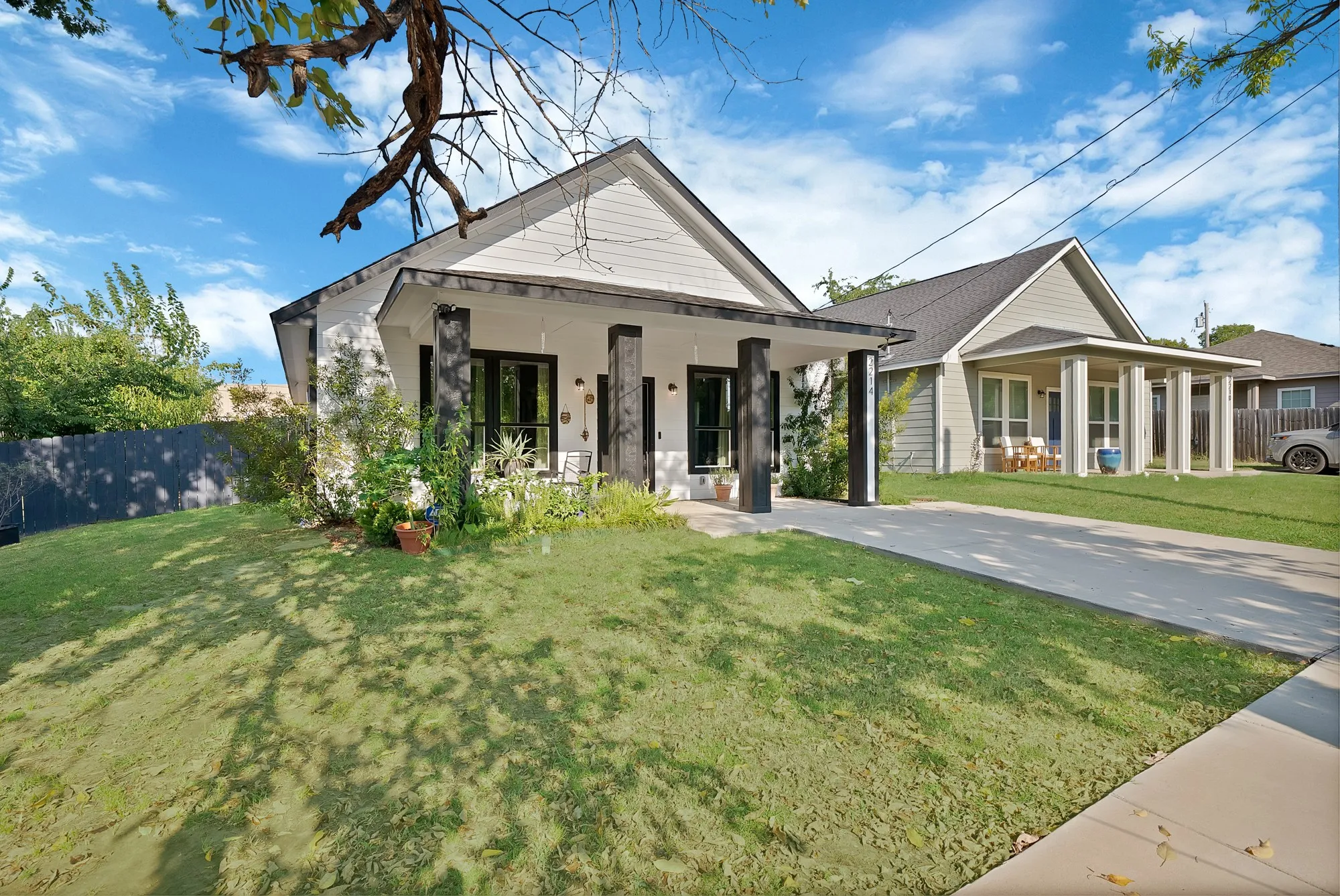 White siding exterior with a dark trim roof, covered front porch, dark support pillars, and a concrete driveway
