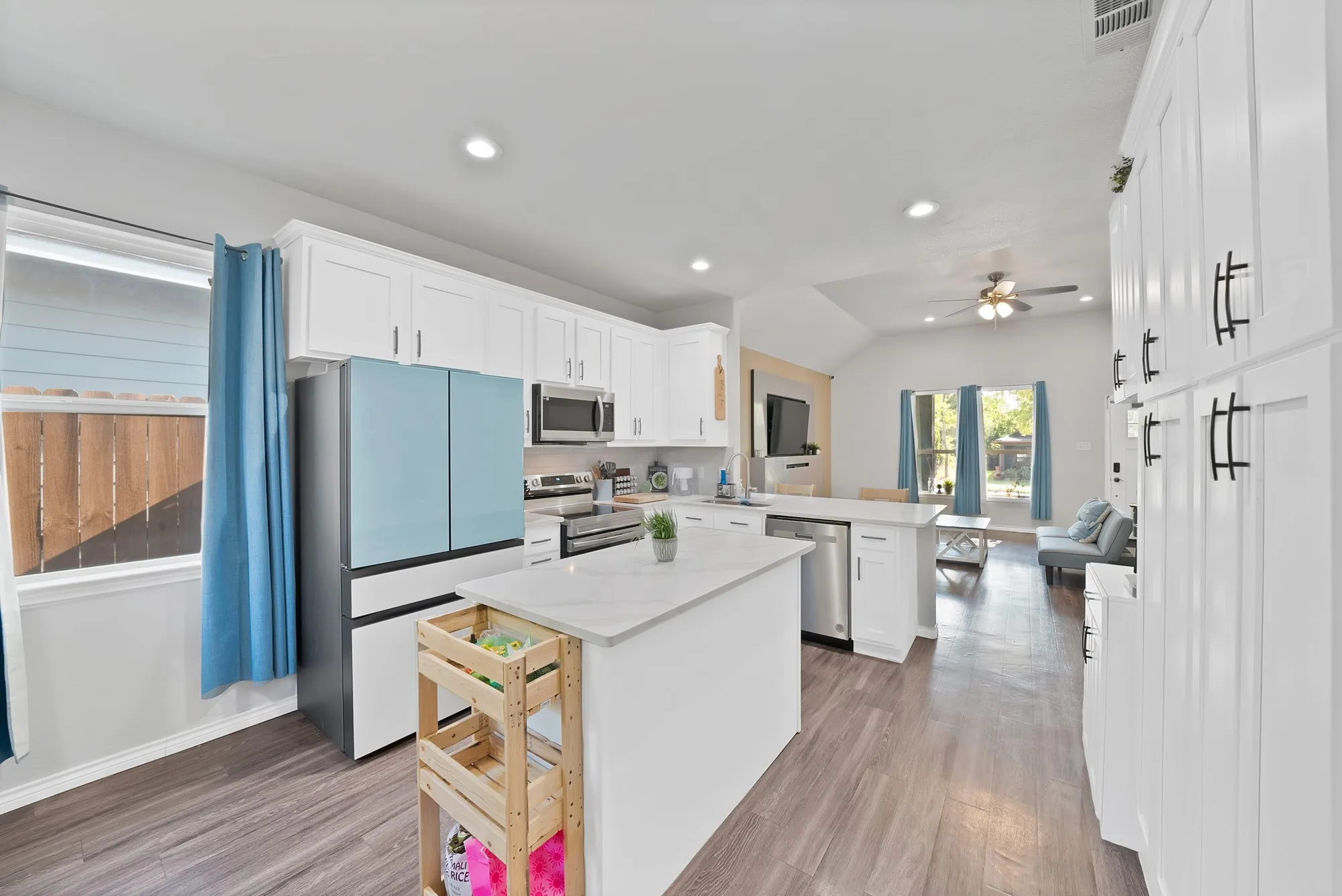 Kitchen featuring white shaker cabinetry, stainless steel appliances, a center island with a light-toned countertop, and wood-finish flooring
