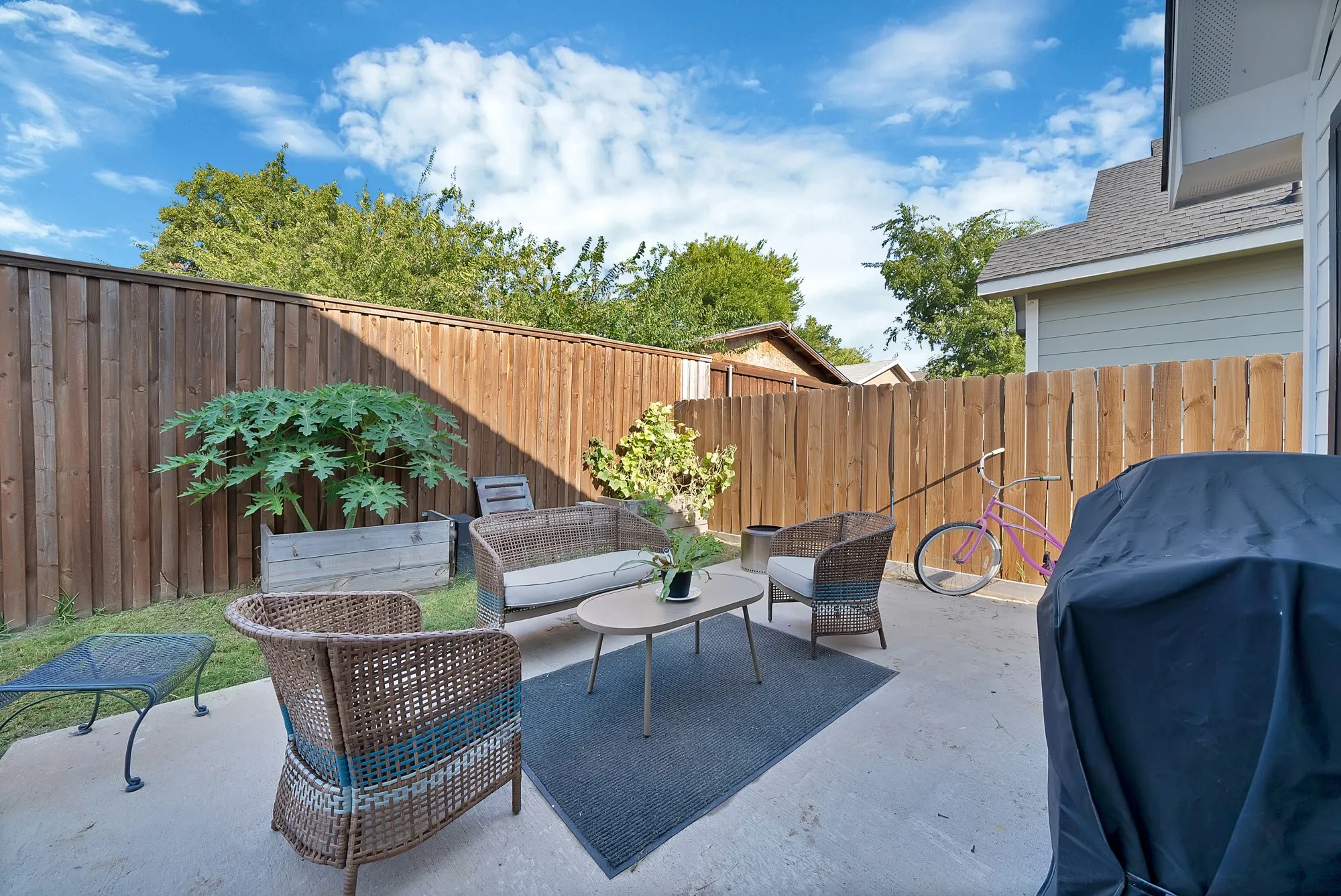 Private backyard featuring a concrete patio, wood privacy fencing, and a grassy area with mature plantings