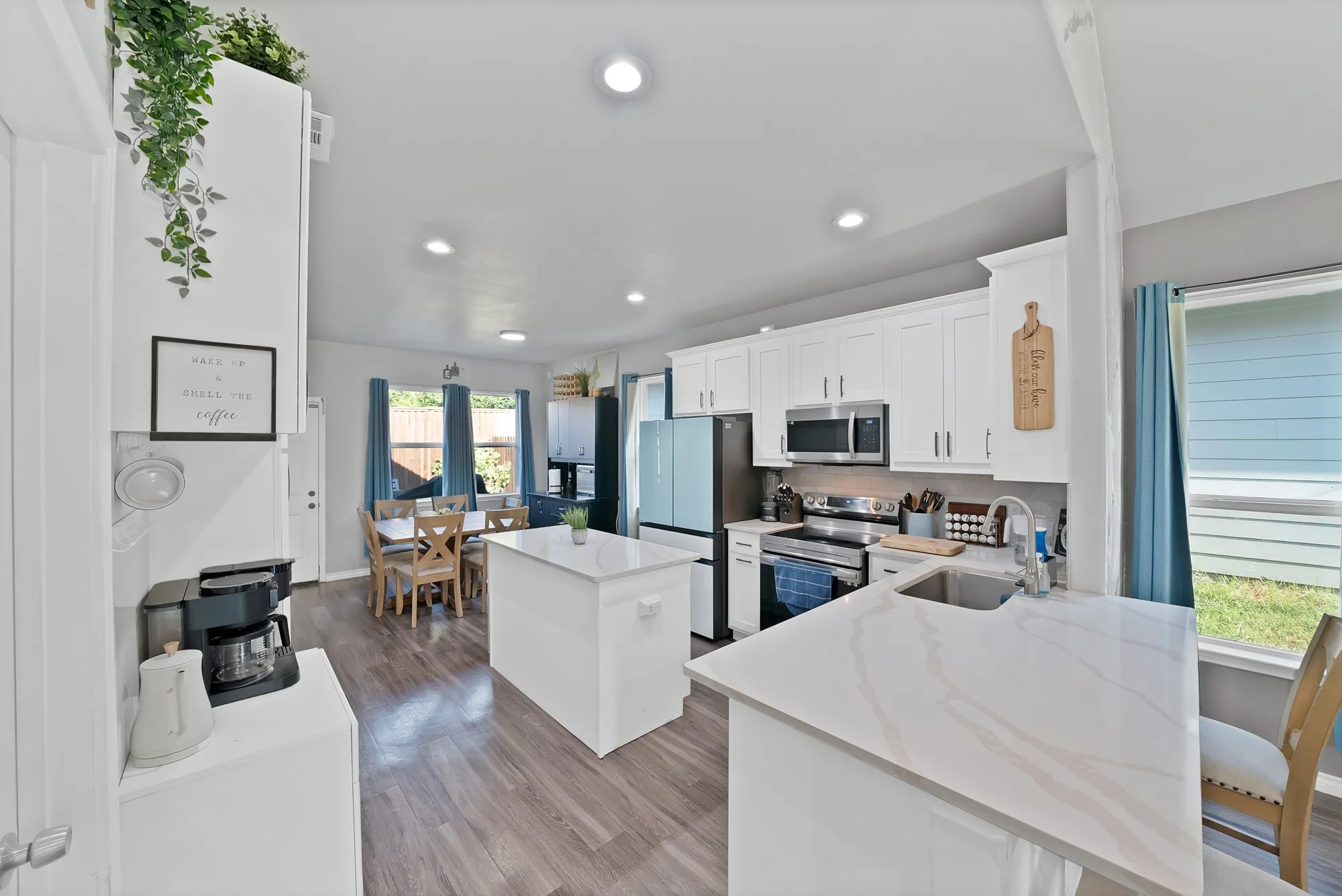 Modern kitchen featuring white cabinetry, stainless steel appliances, light-toned countertops, and wood-finish flooring