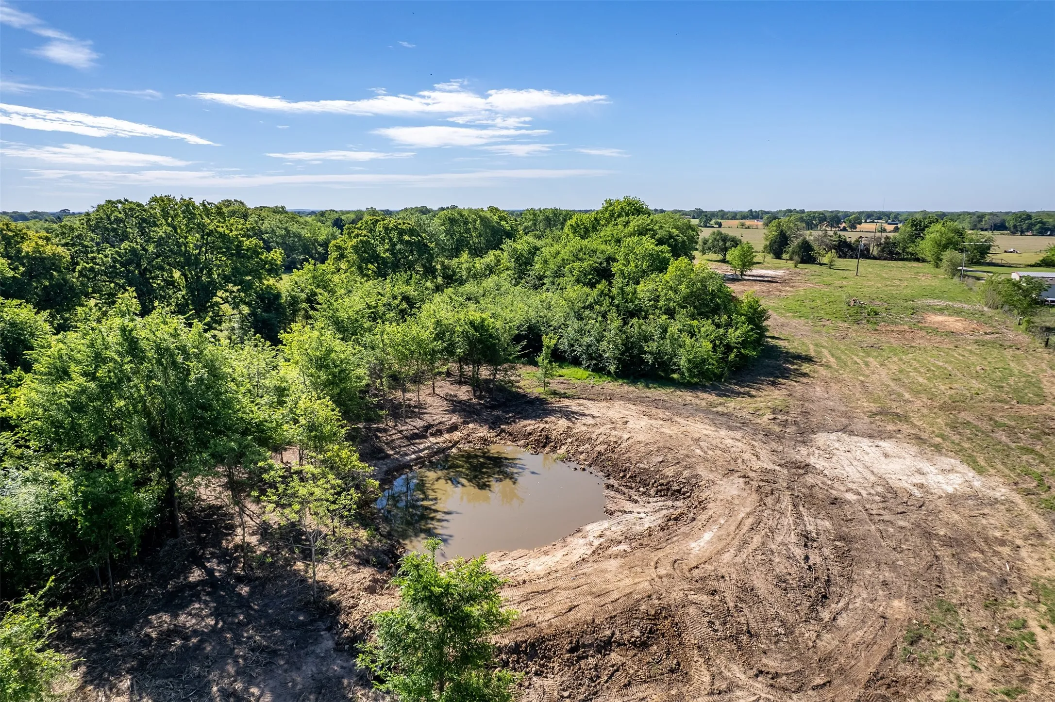 Developed land featuring a pond, surrounding trees, and open fields