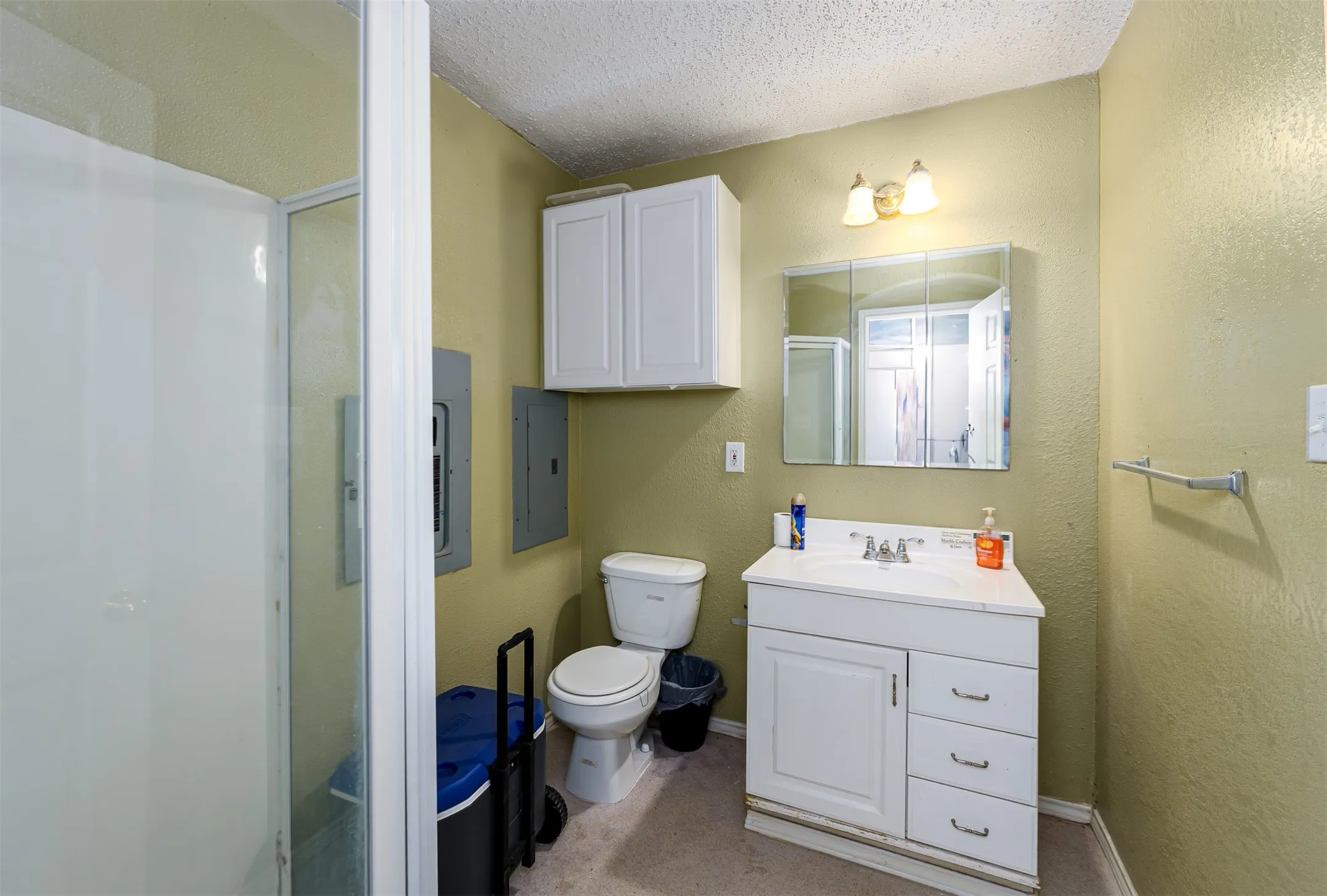 Shower enclosure with a clear glass door, white vanity cabinet with a basin sink, wall-mounted mirrored medicine cabinet, and overhead wall sconce lighting