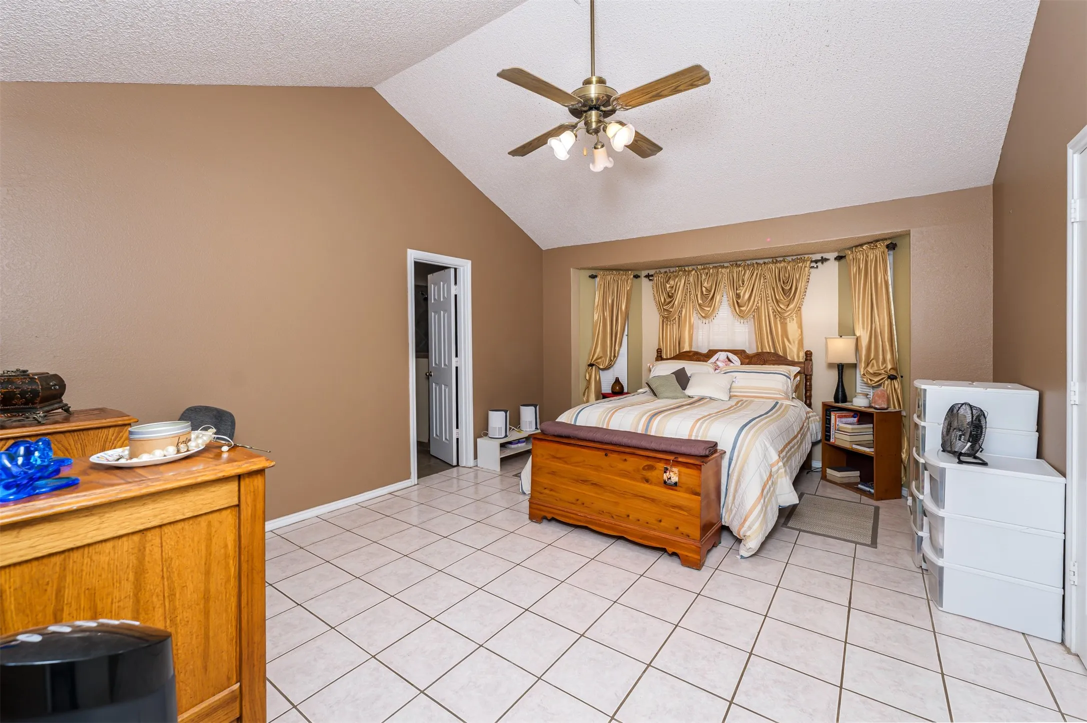 Vaulted ceiling with a brass-finish ceiling fan, recessed bay window, and tile flooring