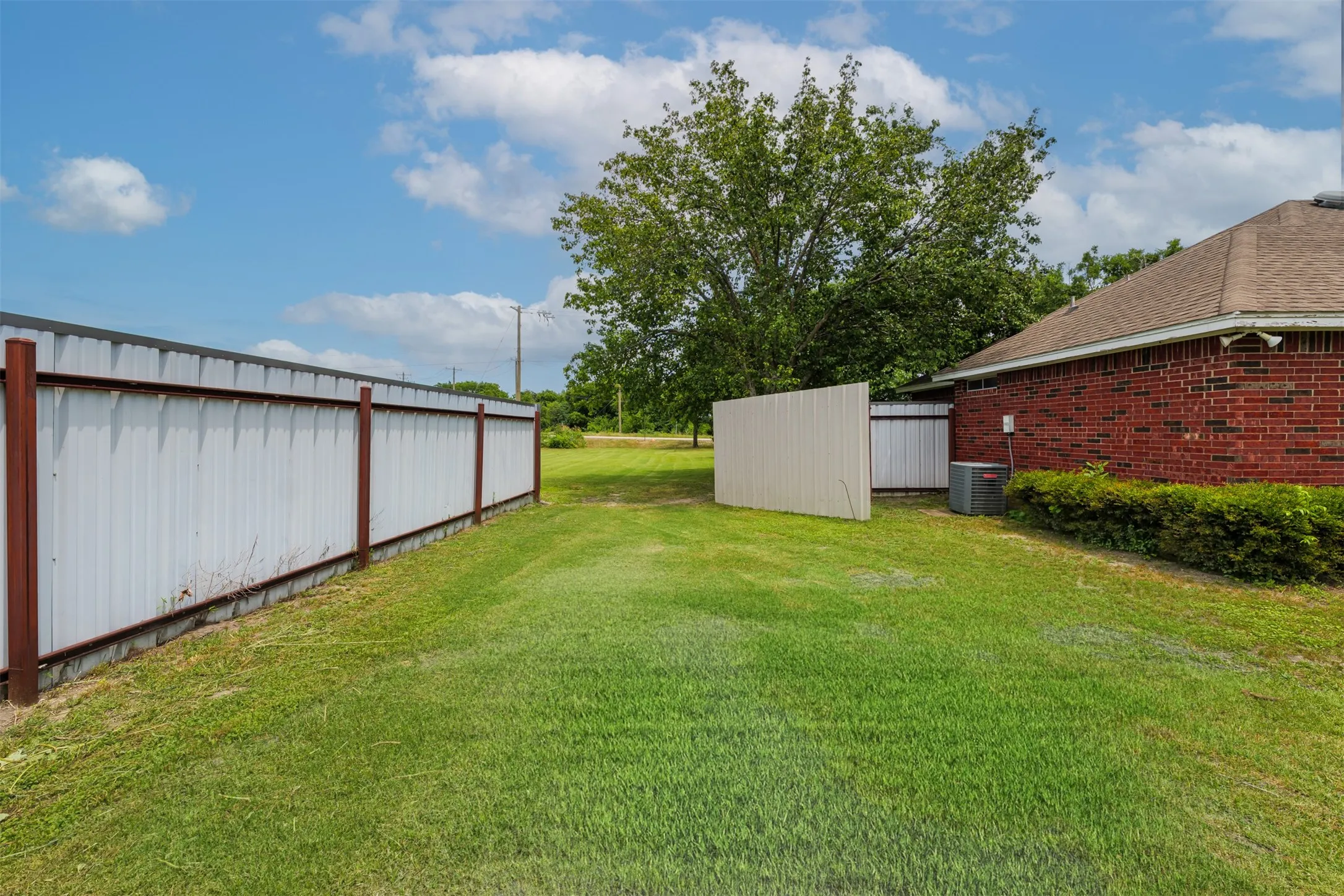 Expansive grassy outdoor space featuring a brick exterior structure and privacy fencing