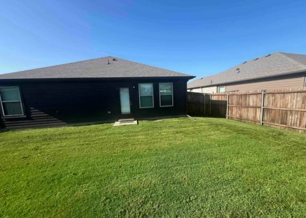 Expansive backyard featuring a manicured lawn, wood fencing, and a rear entry door