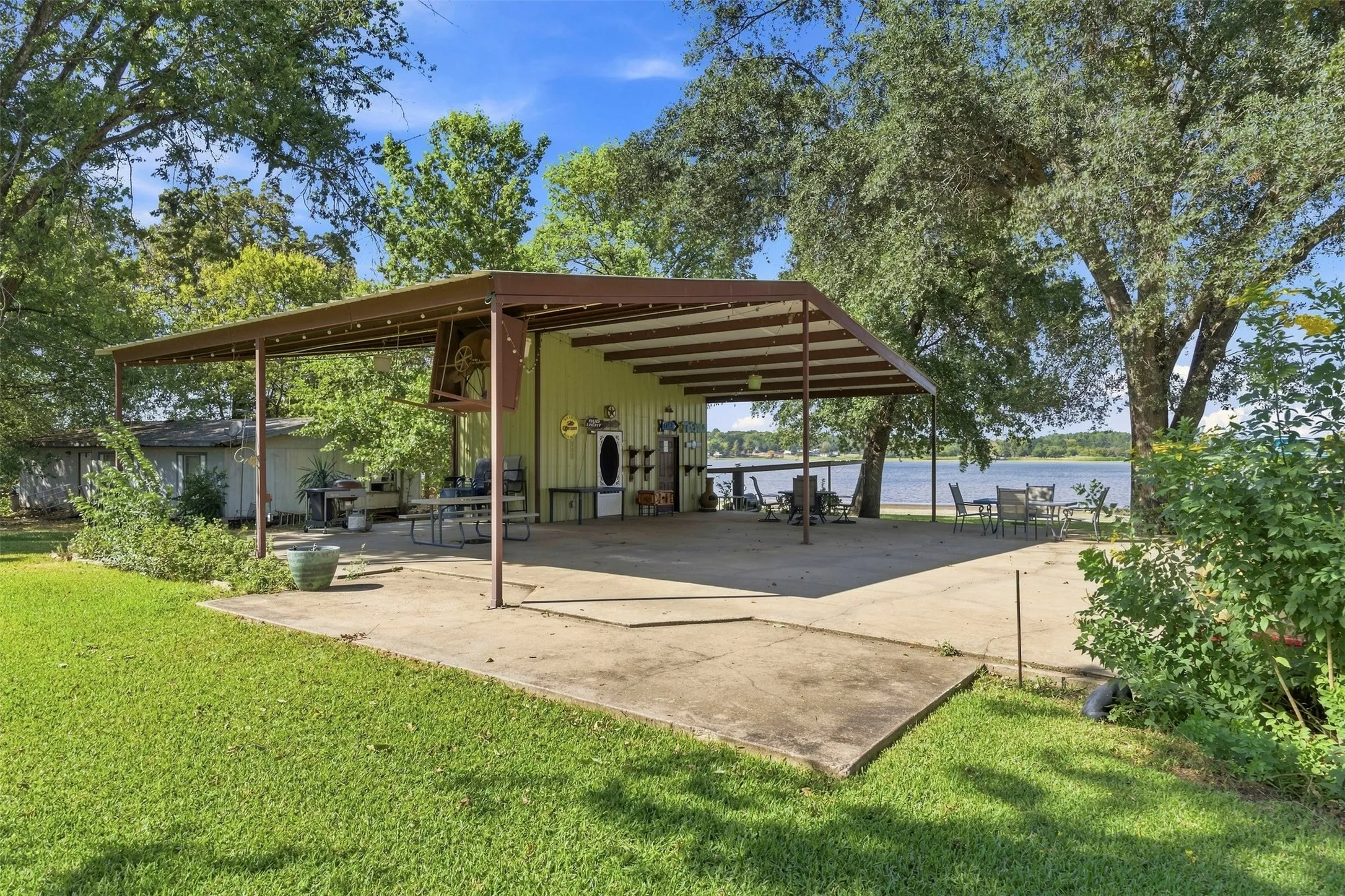 Expansive covered patio with concrete flooring, open-air structure, and water frontage