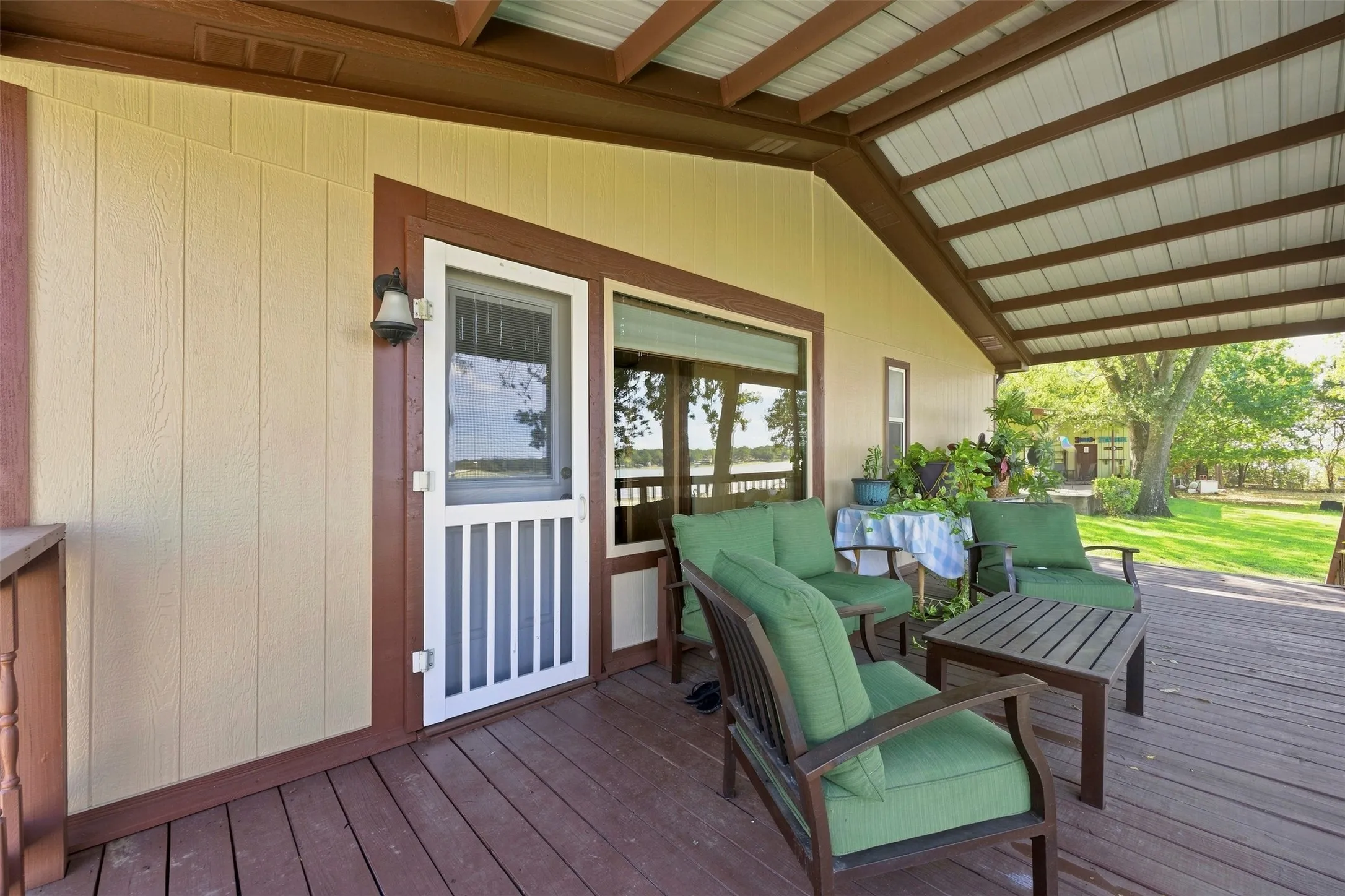 Expansive covered porch featuring a wood deck, exposed beam ceiling, and a screen door