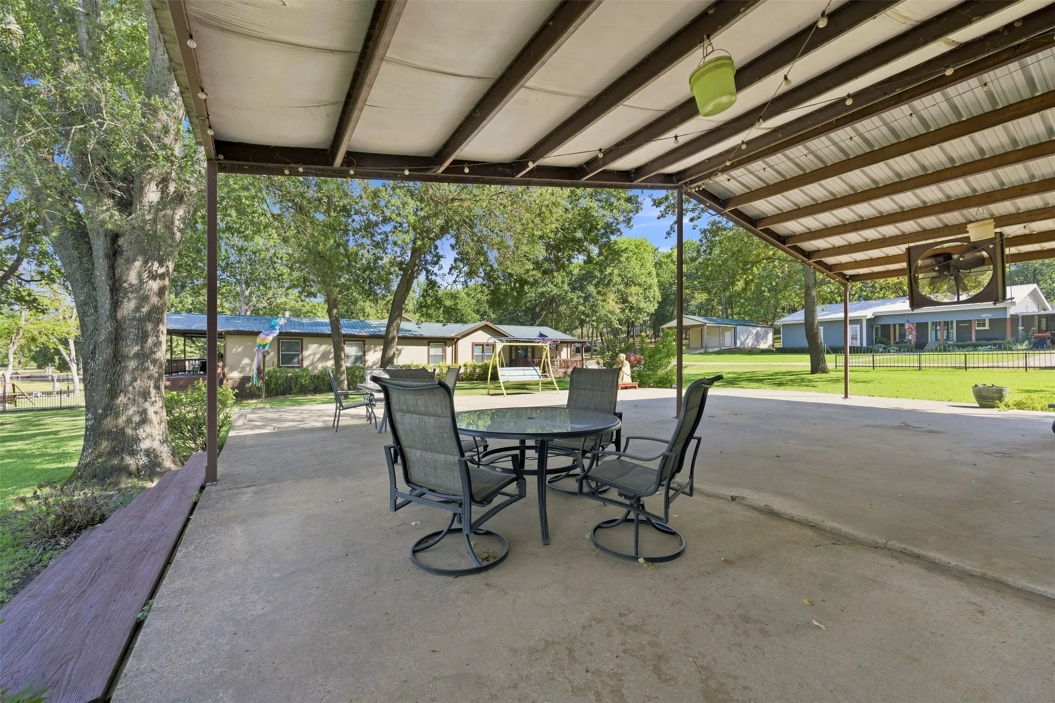 Expansive concrete patio with a metal roof covering, supported by metal posts, and integrated lighting fixtures