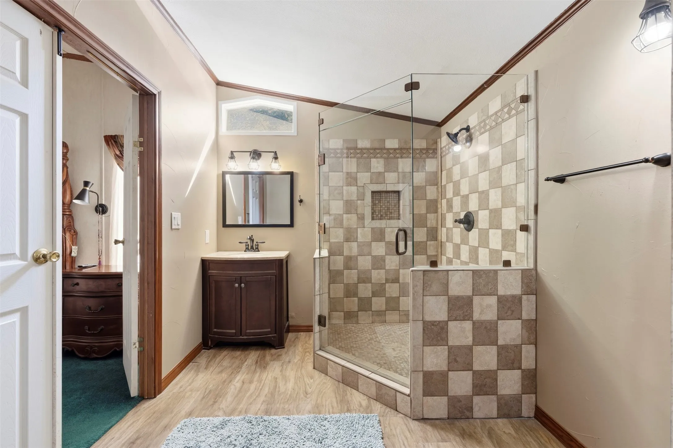 Glass-enclosed shower with checkerboard tiling, wood-finish flooring, dark wood vanity with integrated sink, and bronze fixtures