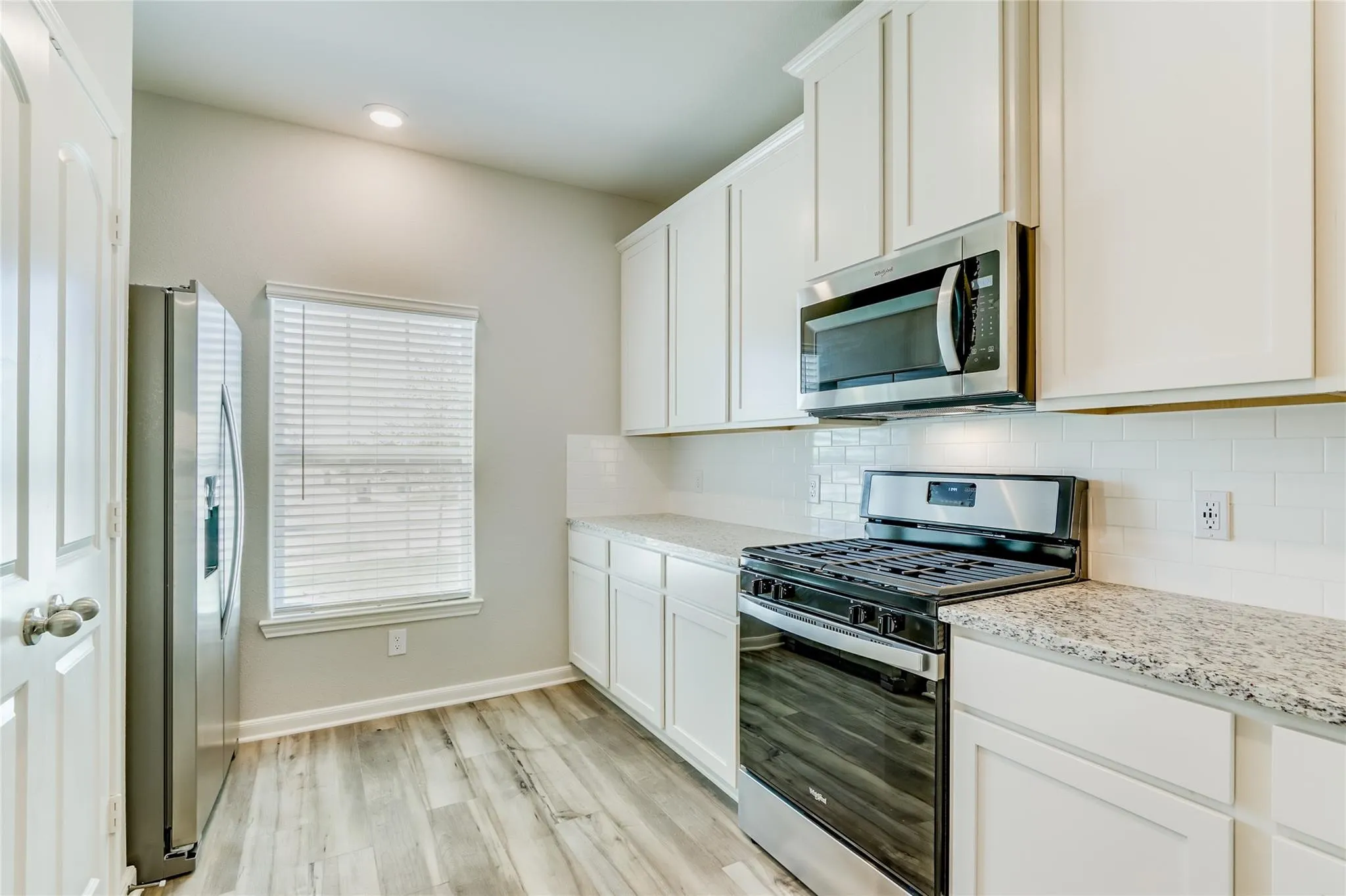 Kitchen featuring white shaker-style cabinetry, granite countertops, stainless steel appliances, a white subway tile backsplash, and wood-finish flooring