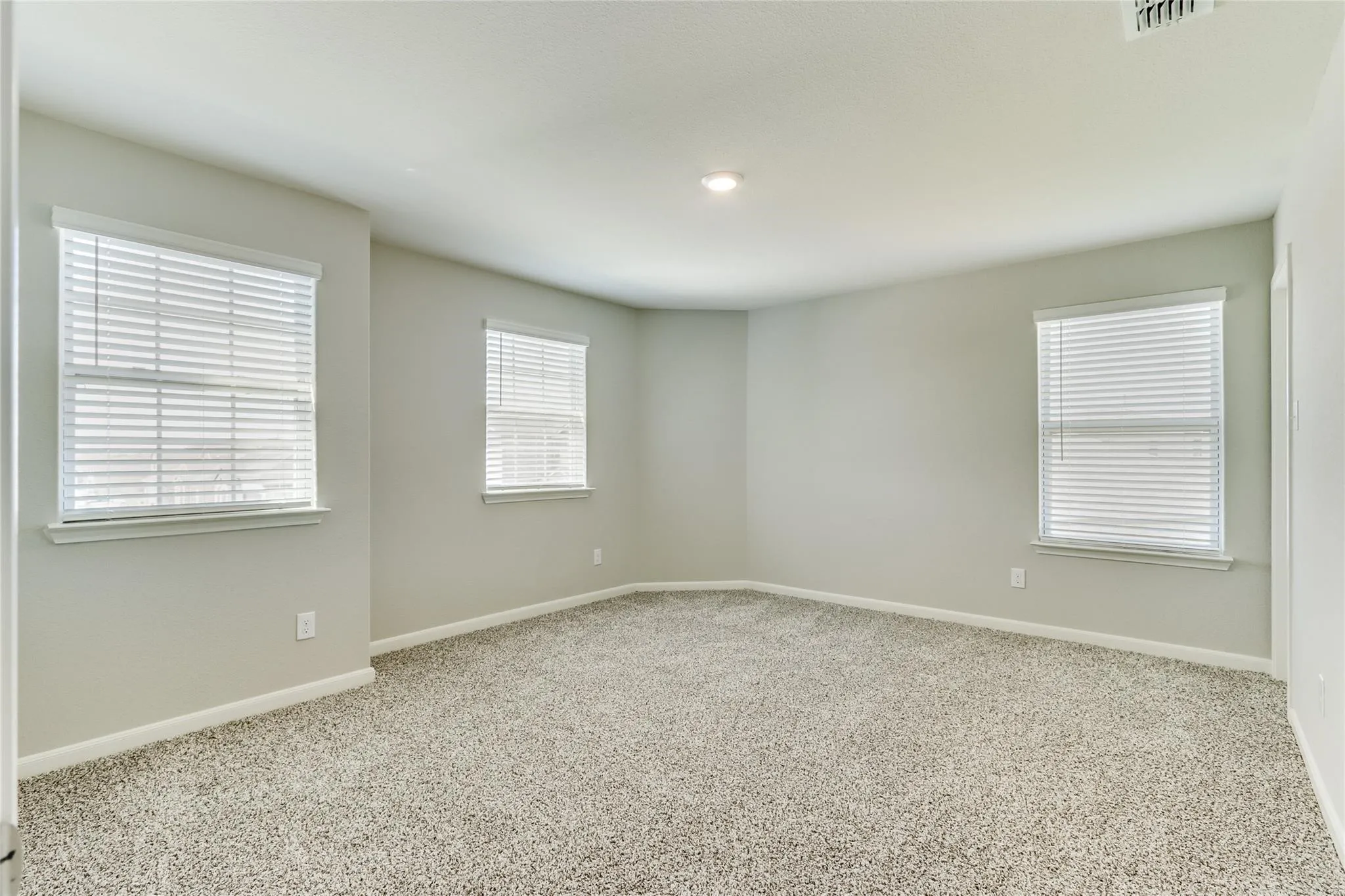 Carpeted room featuring light gray walls, multiple windows with blinds, and recessed lighting