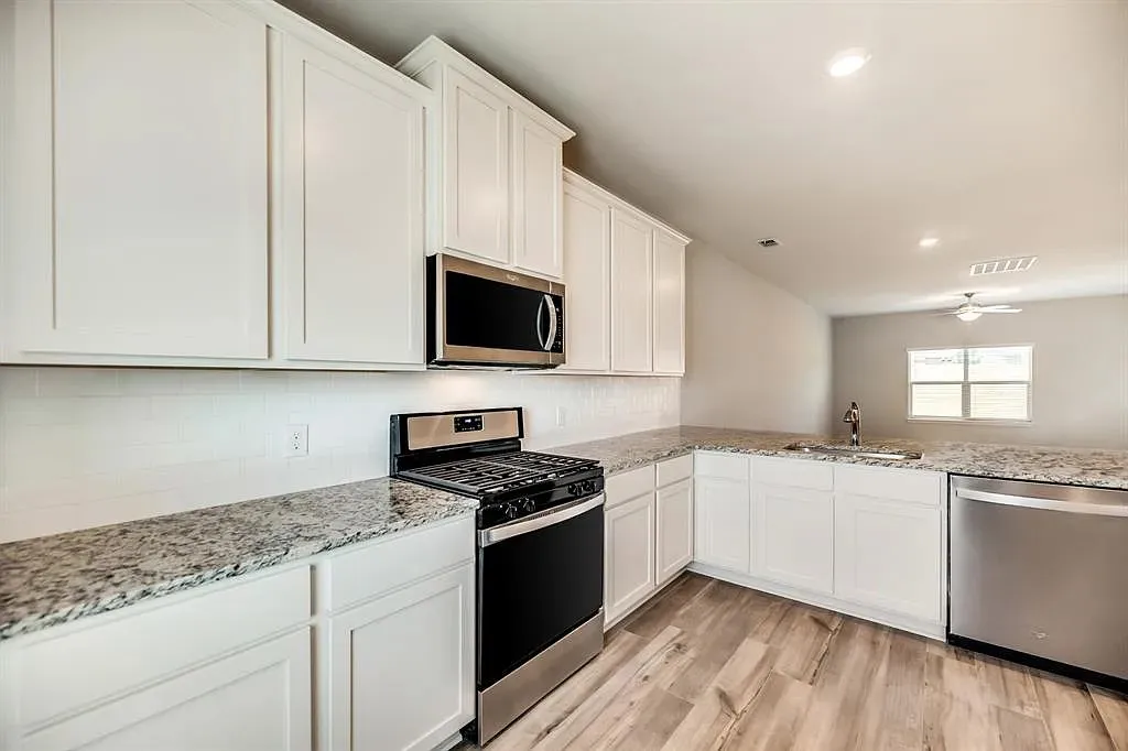 White cabinetry with stainless steel appliances, wood-finish flooring, and light-toned countertops