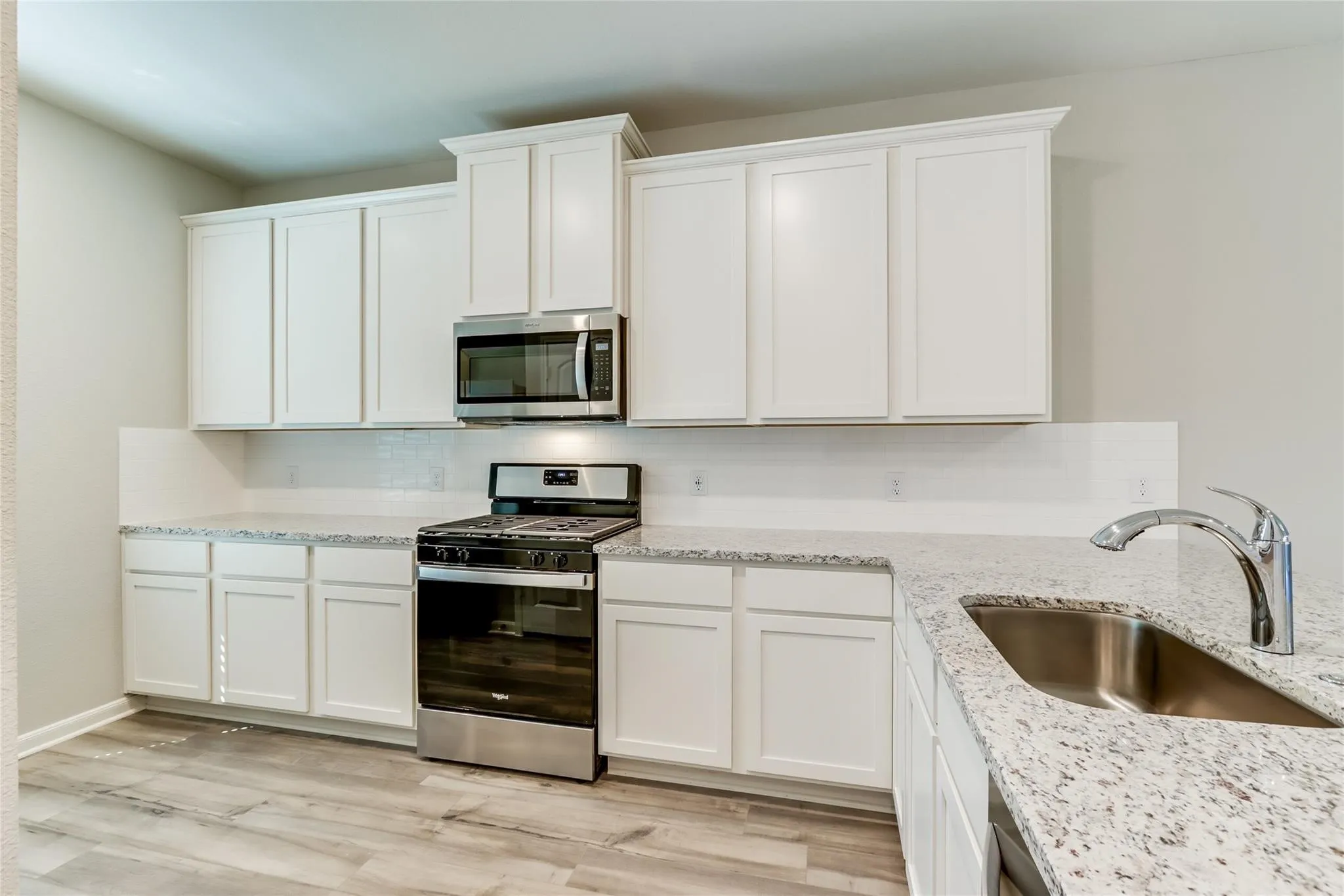 Kitchen featuring white cabinetry, speckled countertops, stainless steel appliances, and wood-finish flooring