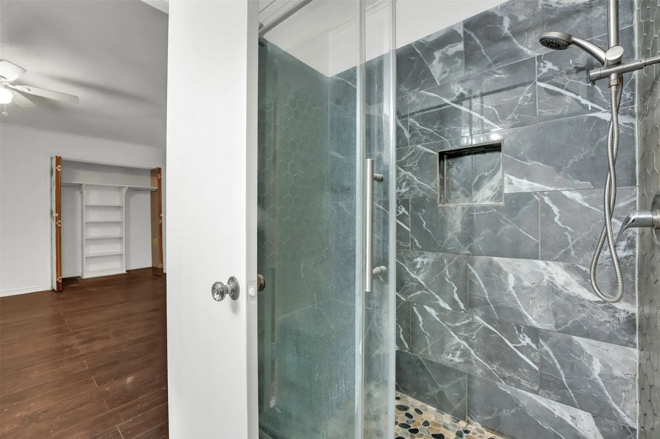 Shower with dark marbled tile walls, integrated shower niche, and a pebble tile floor