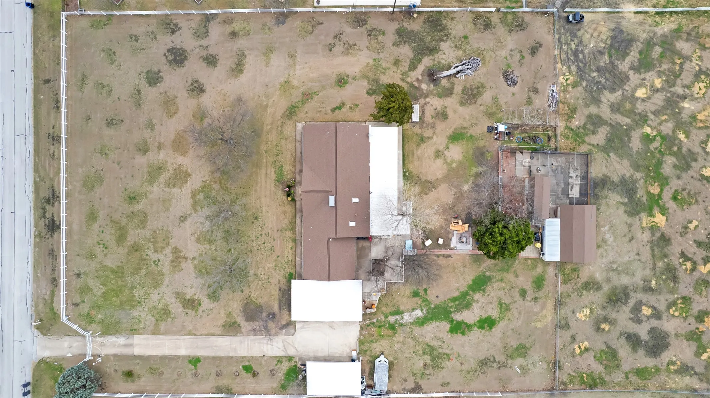 Expansive property featuring a brown roofline, concrete drive, and surrounding fencing