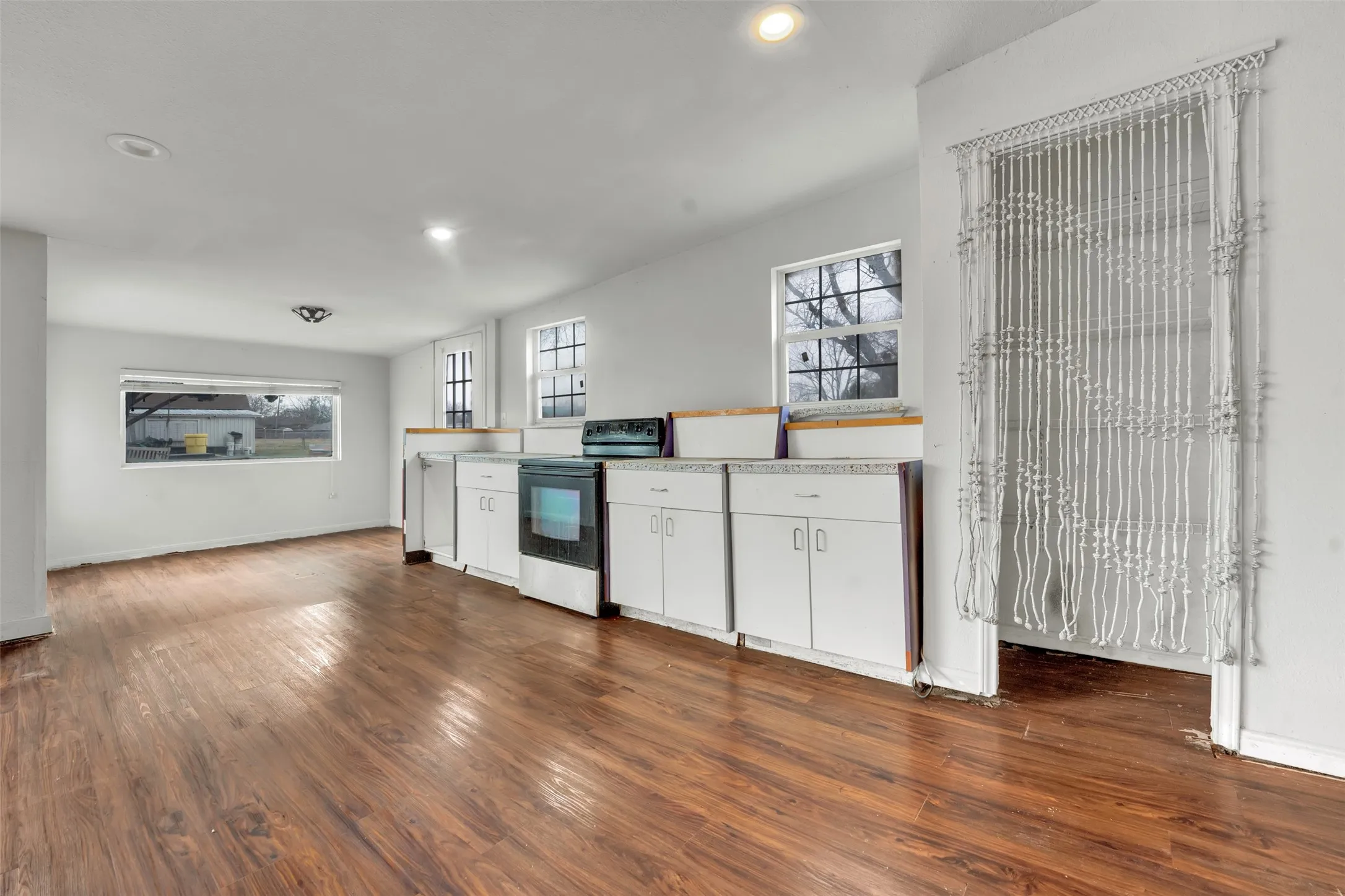 Wood-finish flooring throughout, white cabinetry with silver hardware, recessed lighting, and multiple windows for natural illumination